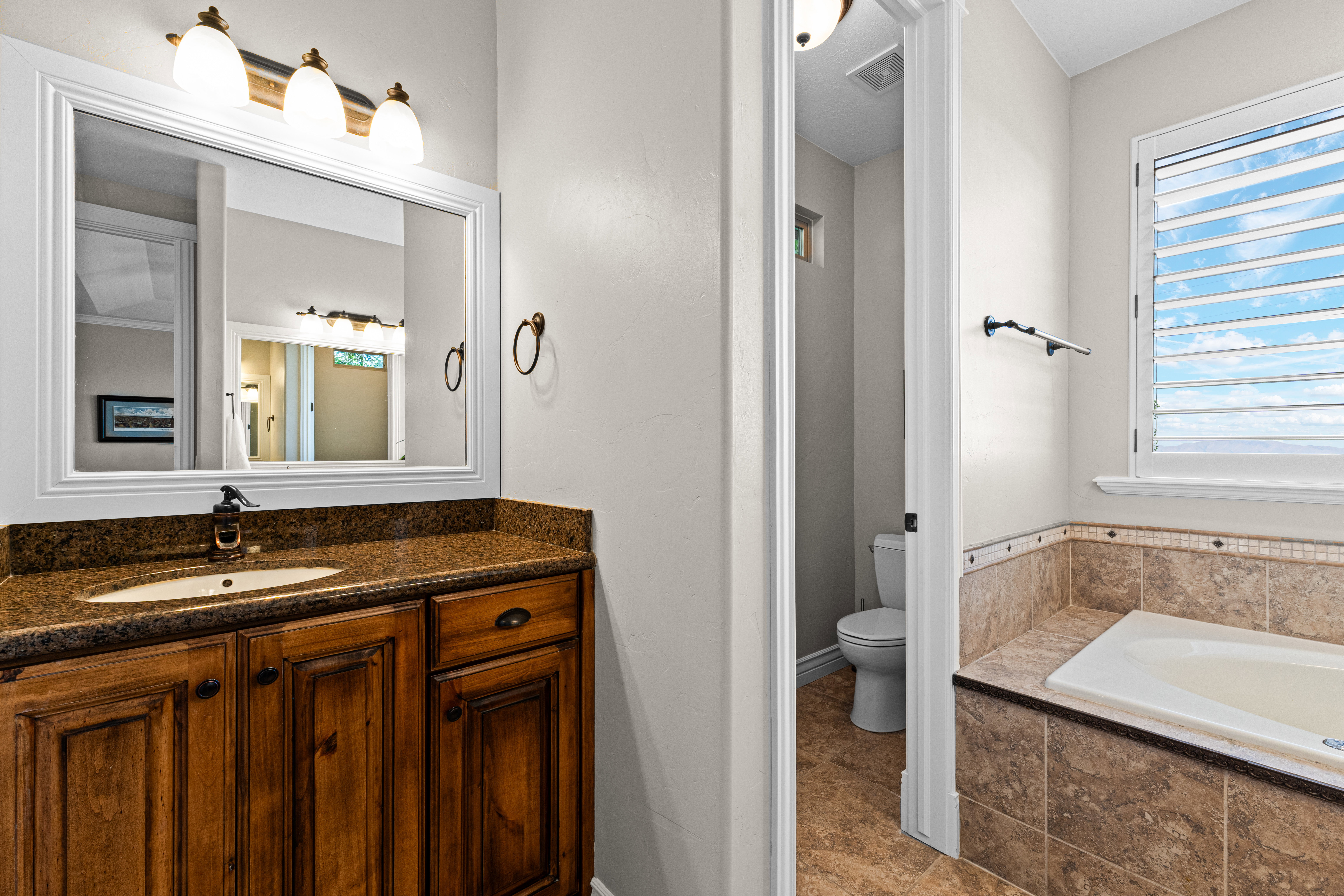 Bathroom featuring a wood-finish vanity with an undermount sink and a speckled countertop, framed mirror, and a three-light vanity fixture