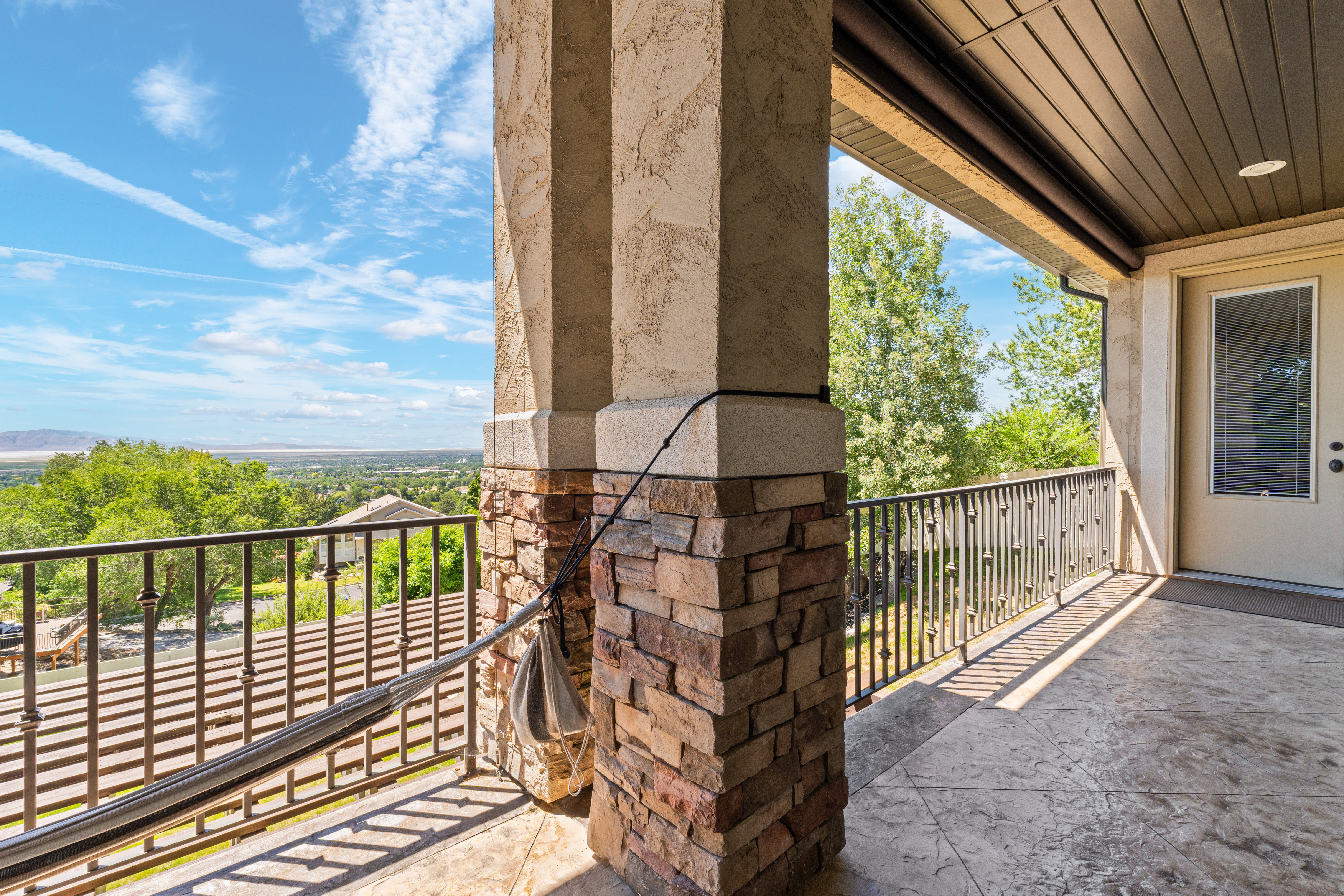 Covered balcony featuring stone and stucco columns, stamped concrete flooring, a wrought iron railing, and a paneled entry door with frosted glass