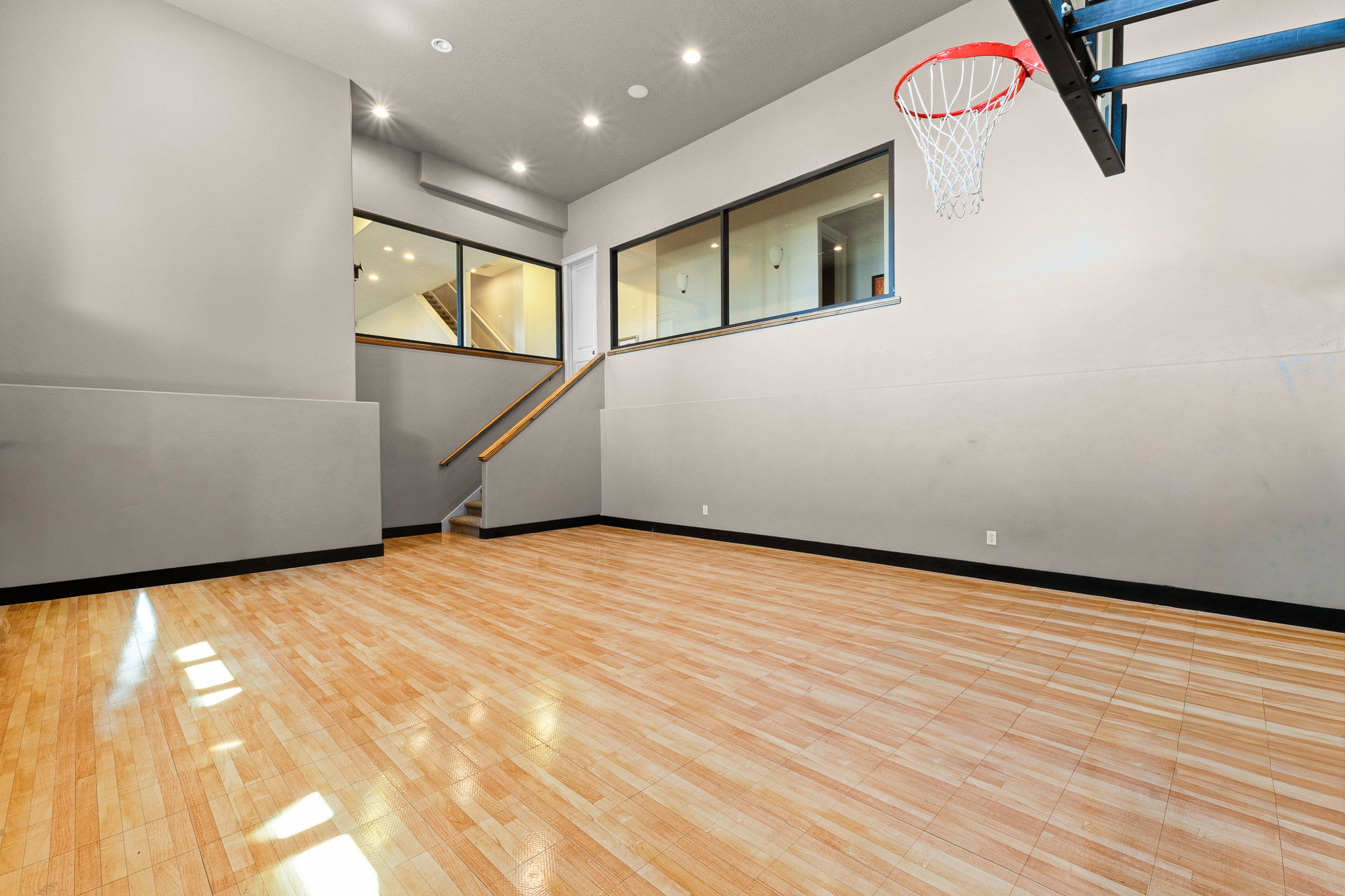 Spacious interior room featuring light wood-finish flooring, recessed ceiling lighting, and a built-in basketball hoop