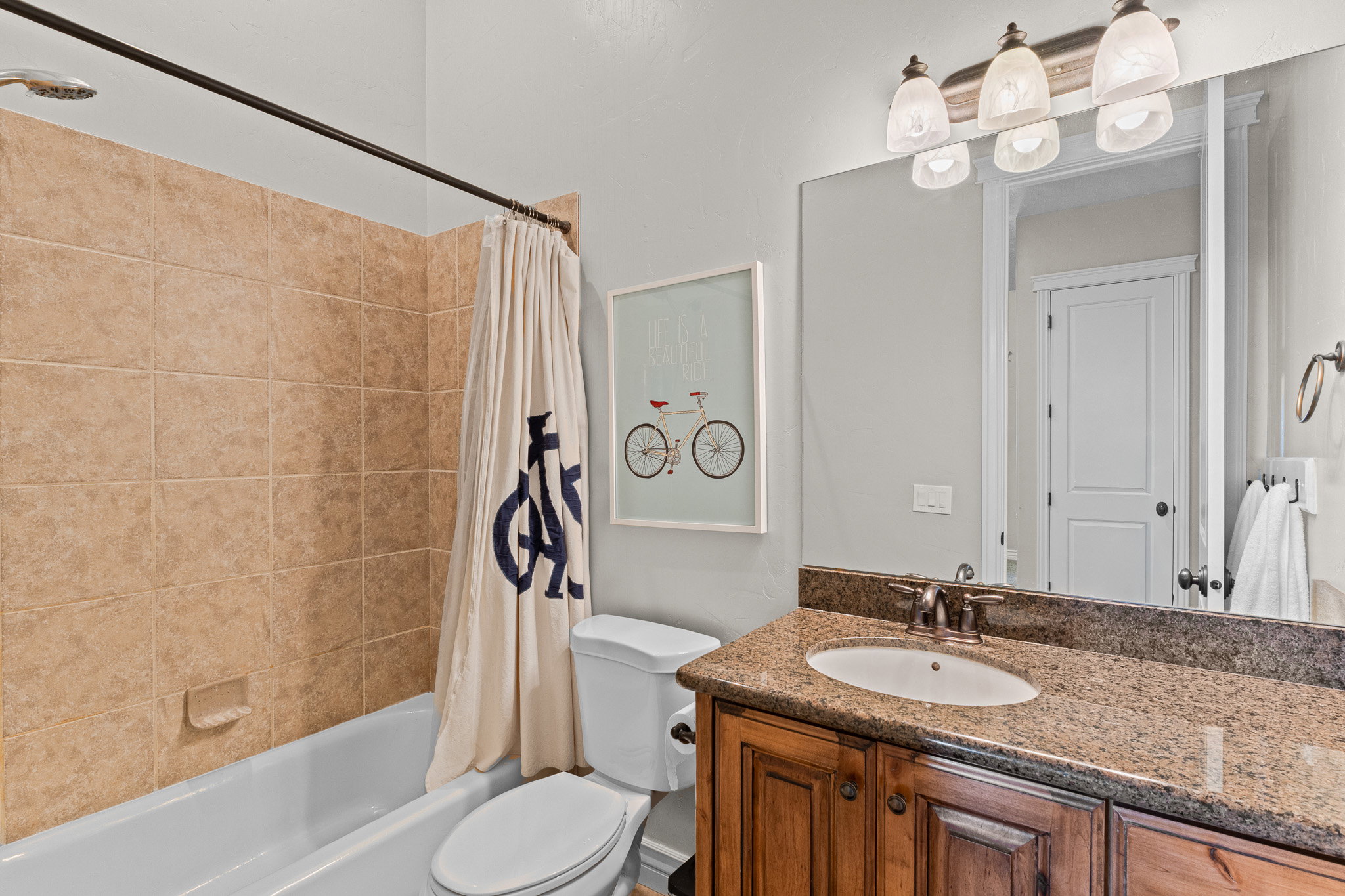 Bathroom featuring a tiled shower surround, integrated bathtub, granite-finish vanity countertop, and a wood-finish vanity cabinet