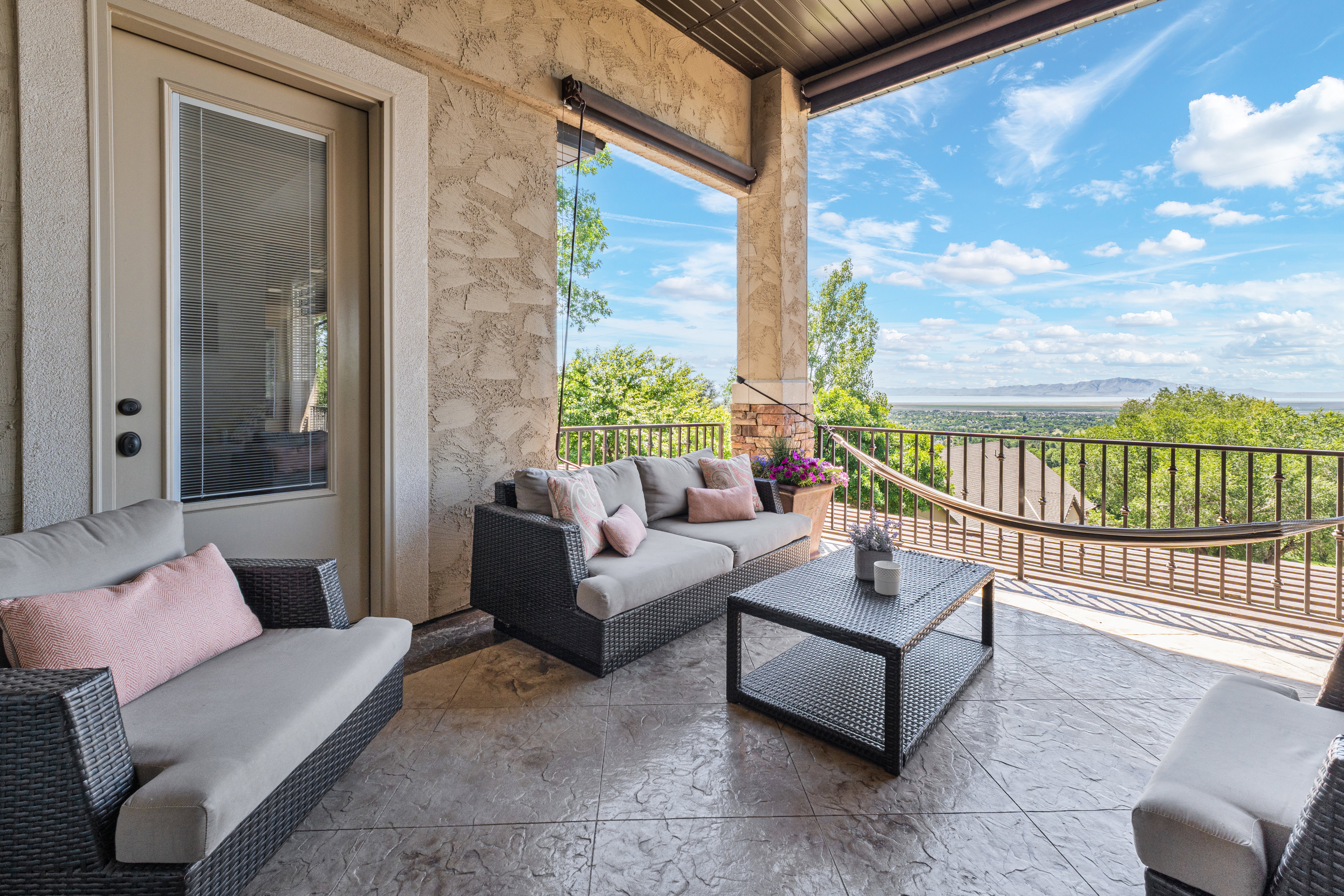 Spacious outdoor balcony featuring stamped concrete flooring, a decorative metal railing, stucco exterior walls, and an elevated ceiling with wood-finish paneling