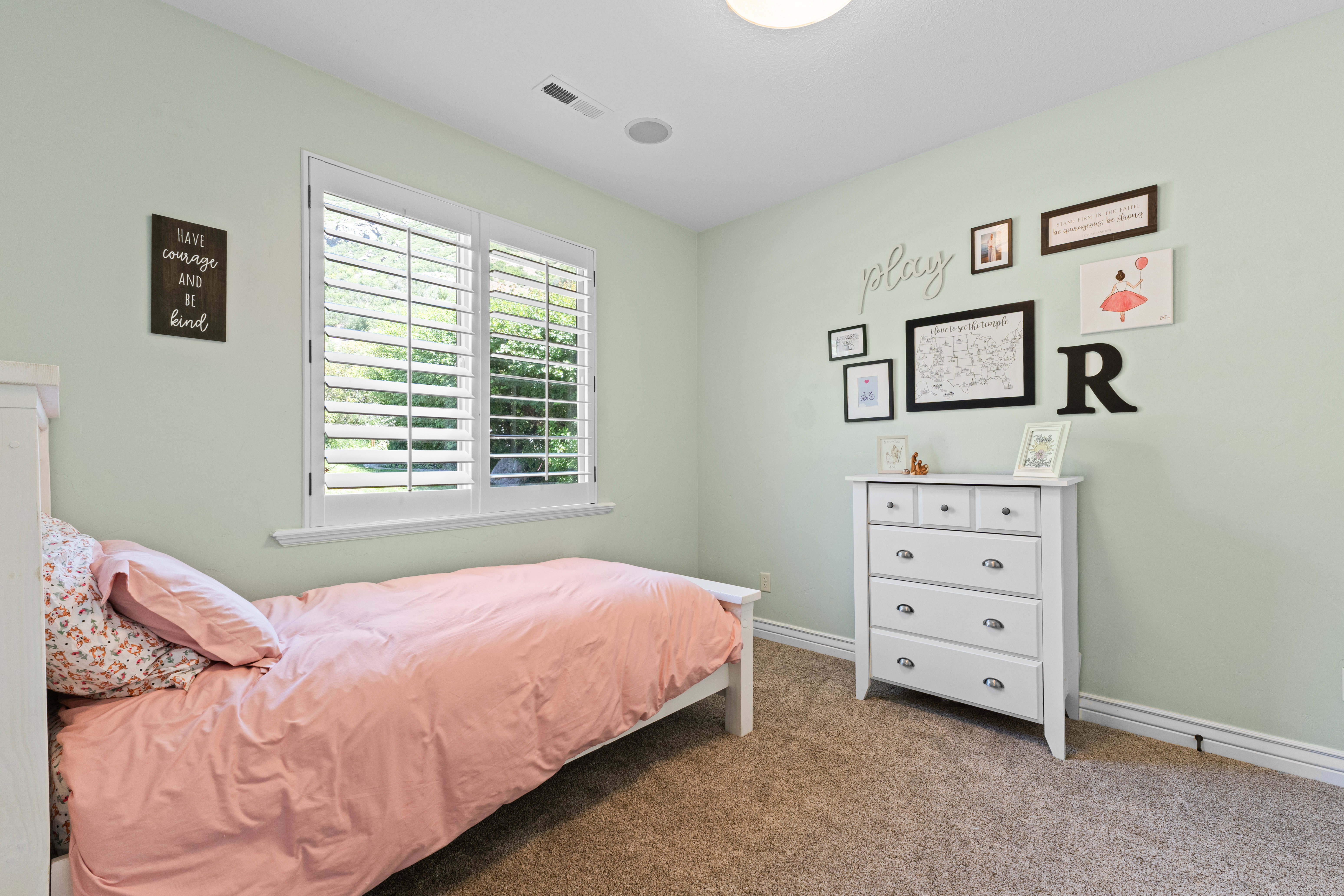 Bedroom featuring a double window with white plantation shutters, light green wall paint, and carpet flooring