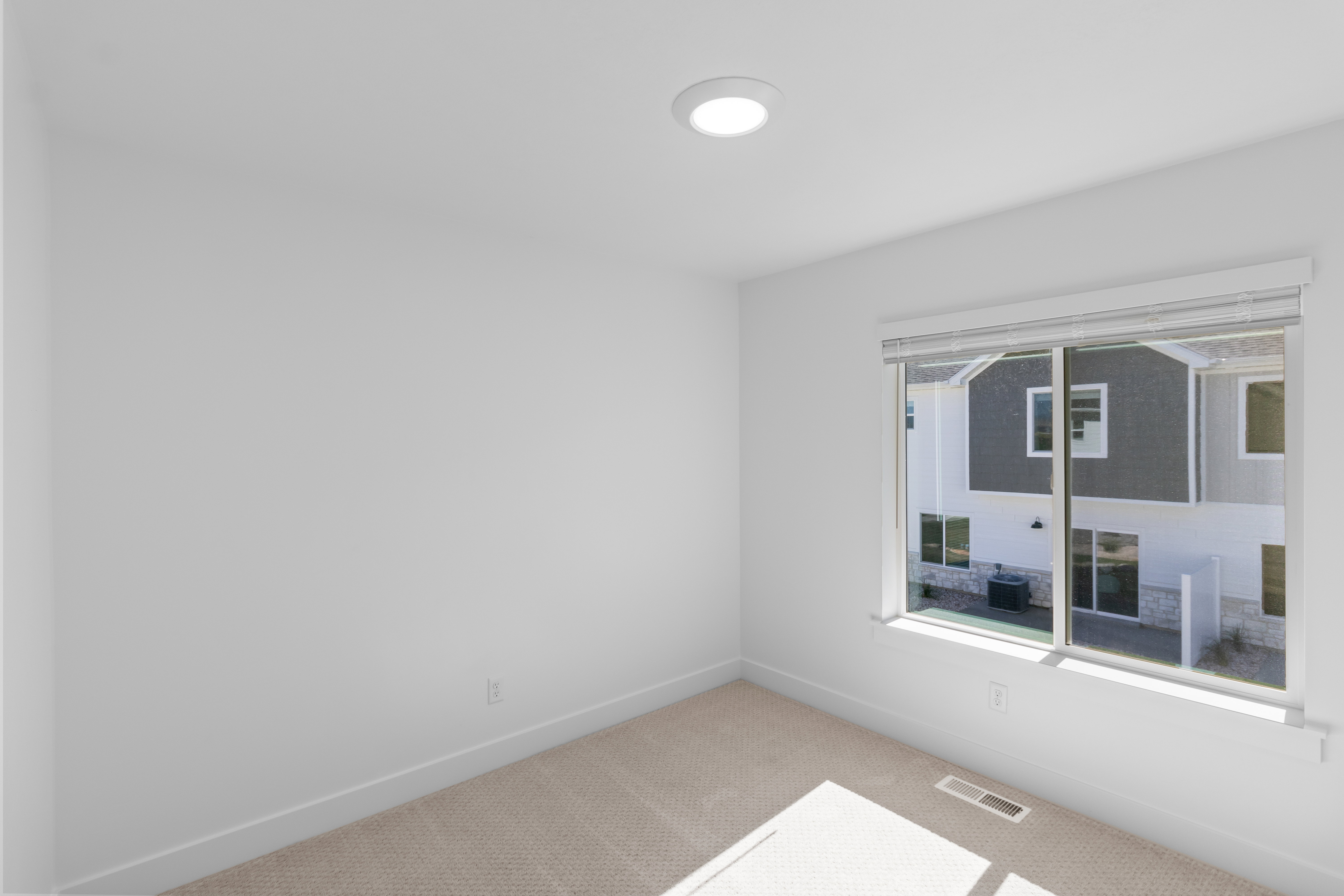 Bright interior space featuring a large window with white blinds, neutral carpeting, and a flush-mount ceiling light fixture