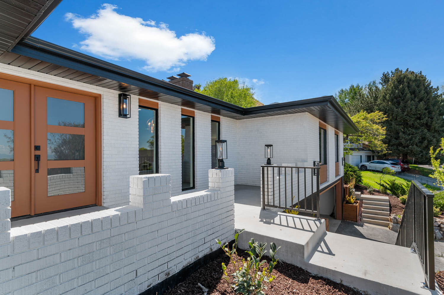 Exterior featuring white painted brick, dual entry doors with frosted glass panels, black-framed windows, and modern outdoor lighting fixtures