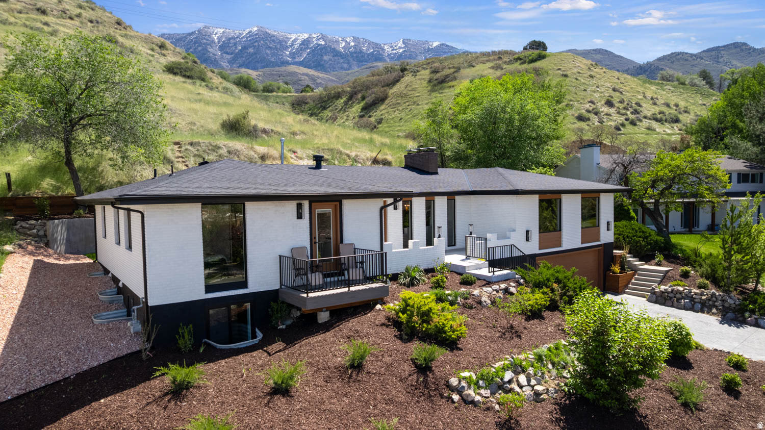 Contemporary exterior featuring white and dark siding, a black shingle roof, a balcony with metal railings, and a terraced front yard with landscaping