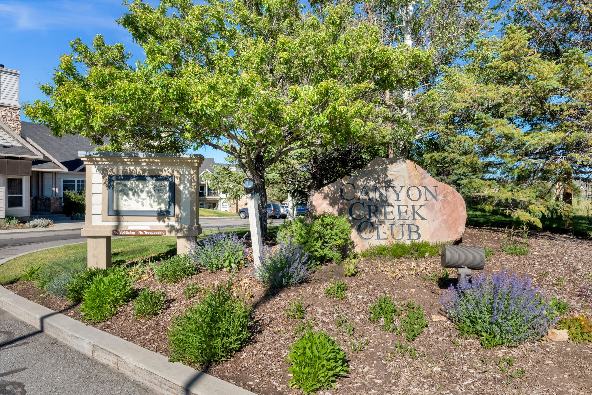 Landscaped entry featuring a large stone monument, decorative sign structure, and mature trees