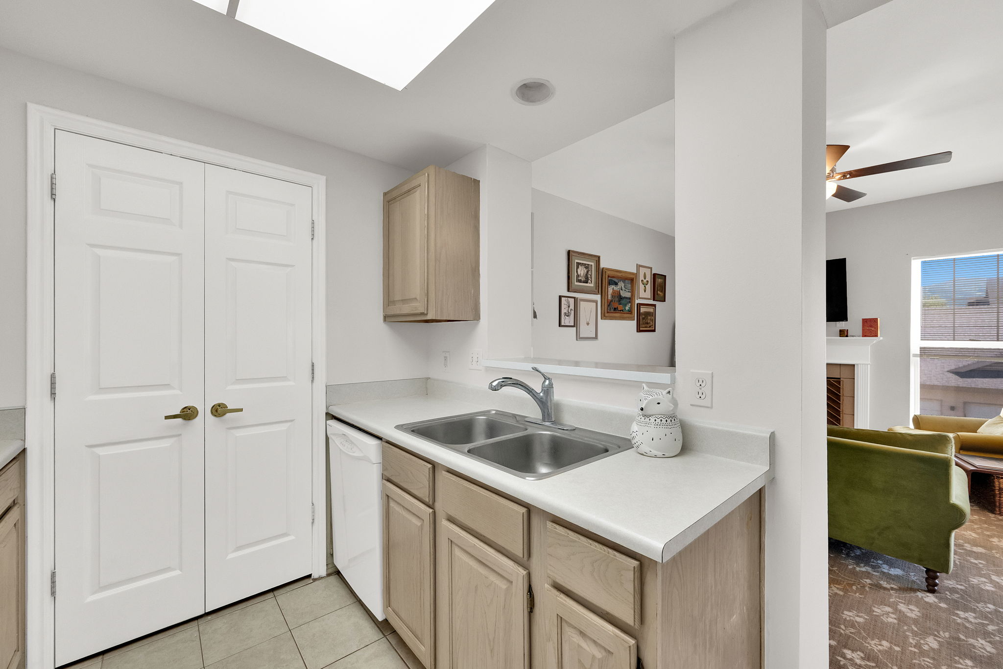 Kitchen featuring a dual basin sink with chrome faucet, light wood-finish cabinetry, and white countertops