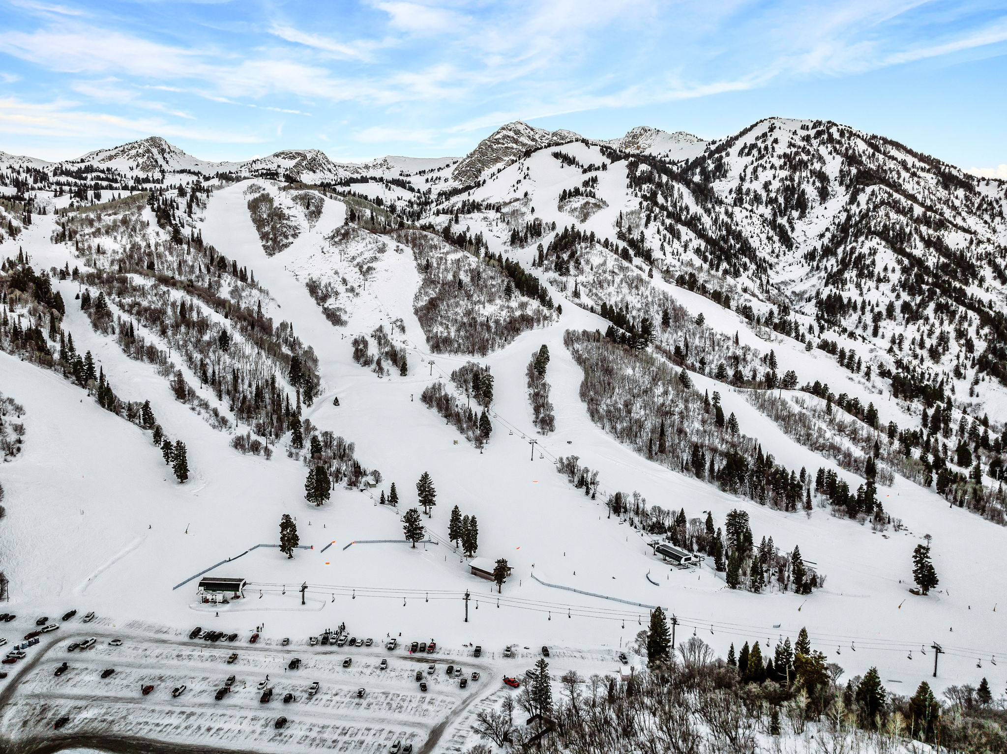 Snow-covered mountain ski terrain featuring multiple ski runs, dense evergreen tree coverage, and ski lift infrastructure