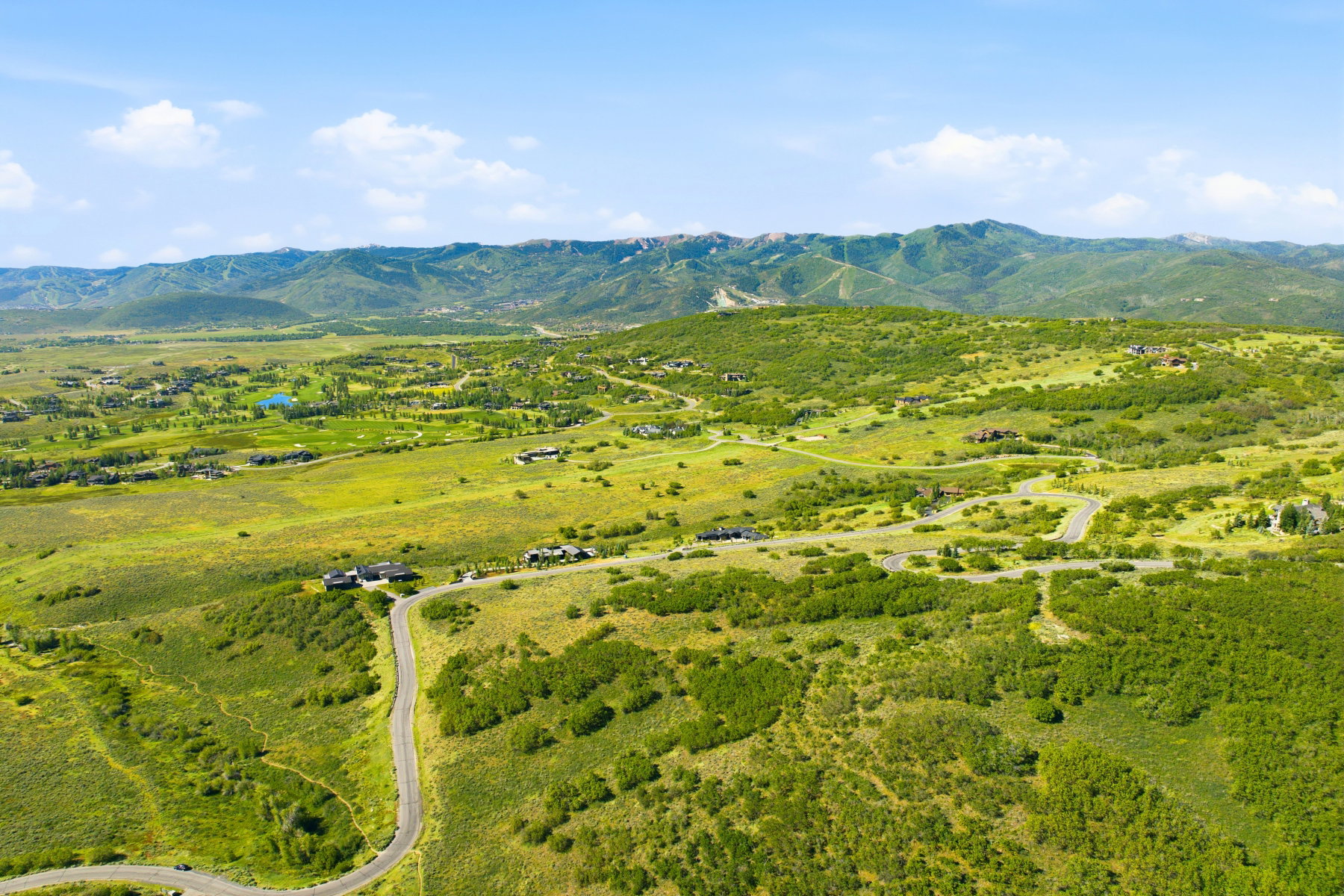 Expansive mountain valley landscape featuring scattered residential properties, winding roads, and abundant green foliage