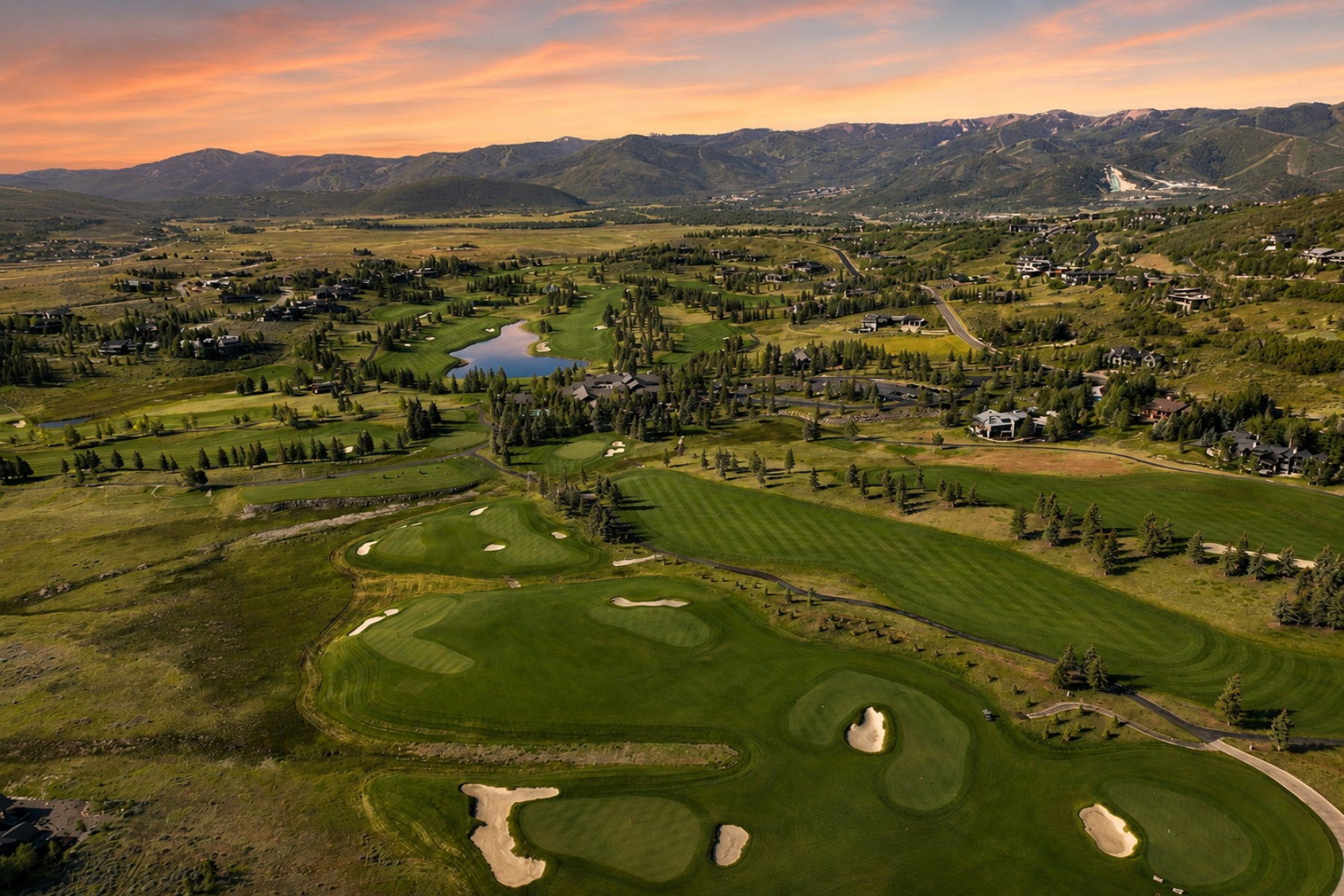 Expansive golf course setting featuring manicured fairways and greens, sand traps, and a central pond