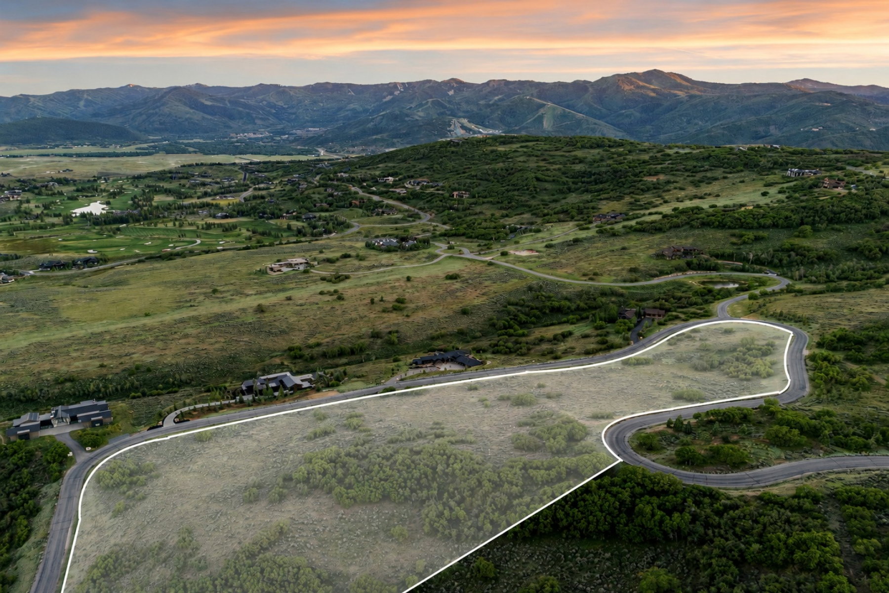 Expansive land parcel featuring a winding paved road, surrounding lush greenery, and distant mountain ranges