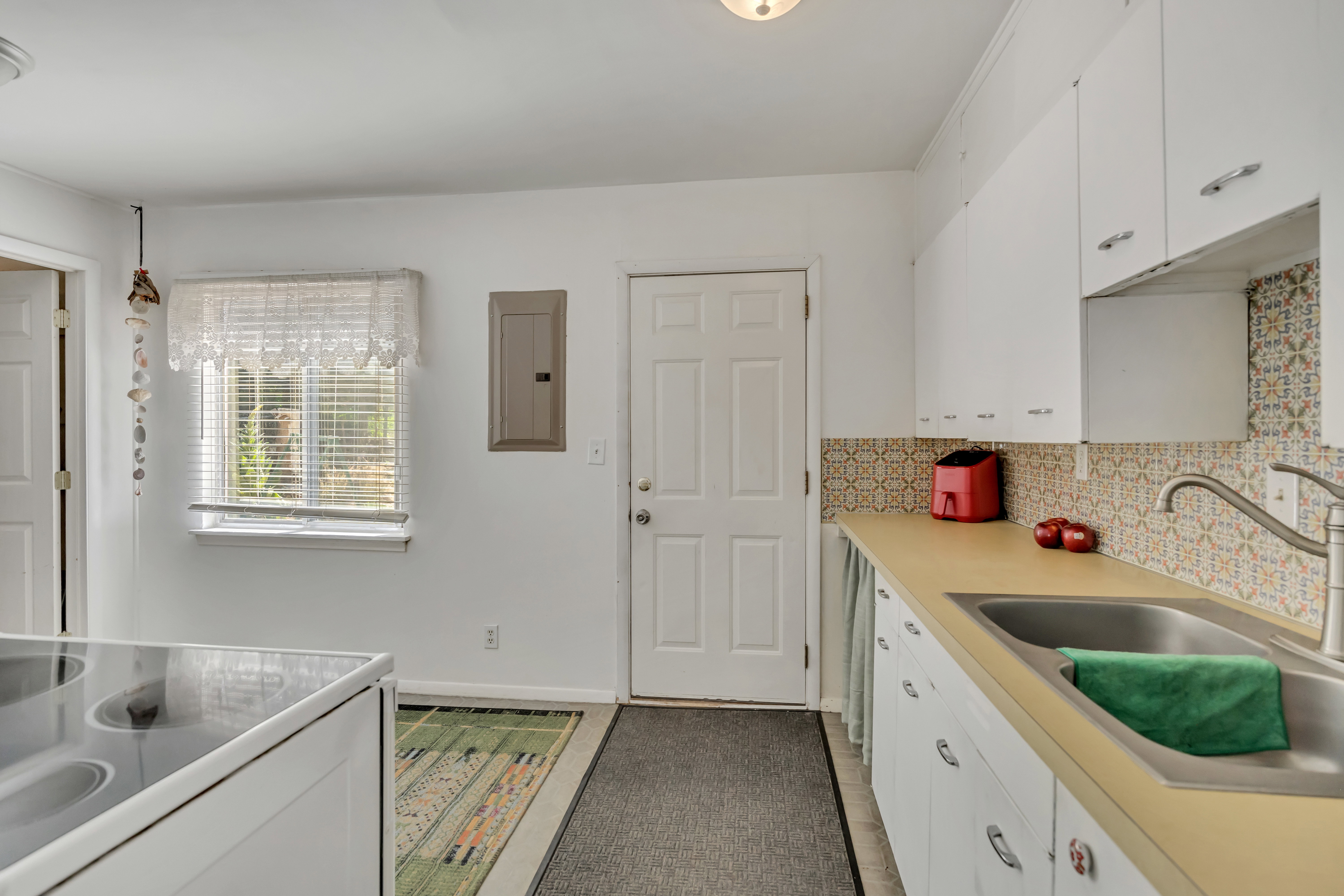 Kitchen featuring white cabinetry, a single basin stainless steel sink, a patterned tile backsplash, and a window with blinds
