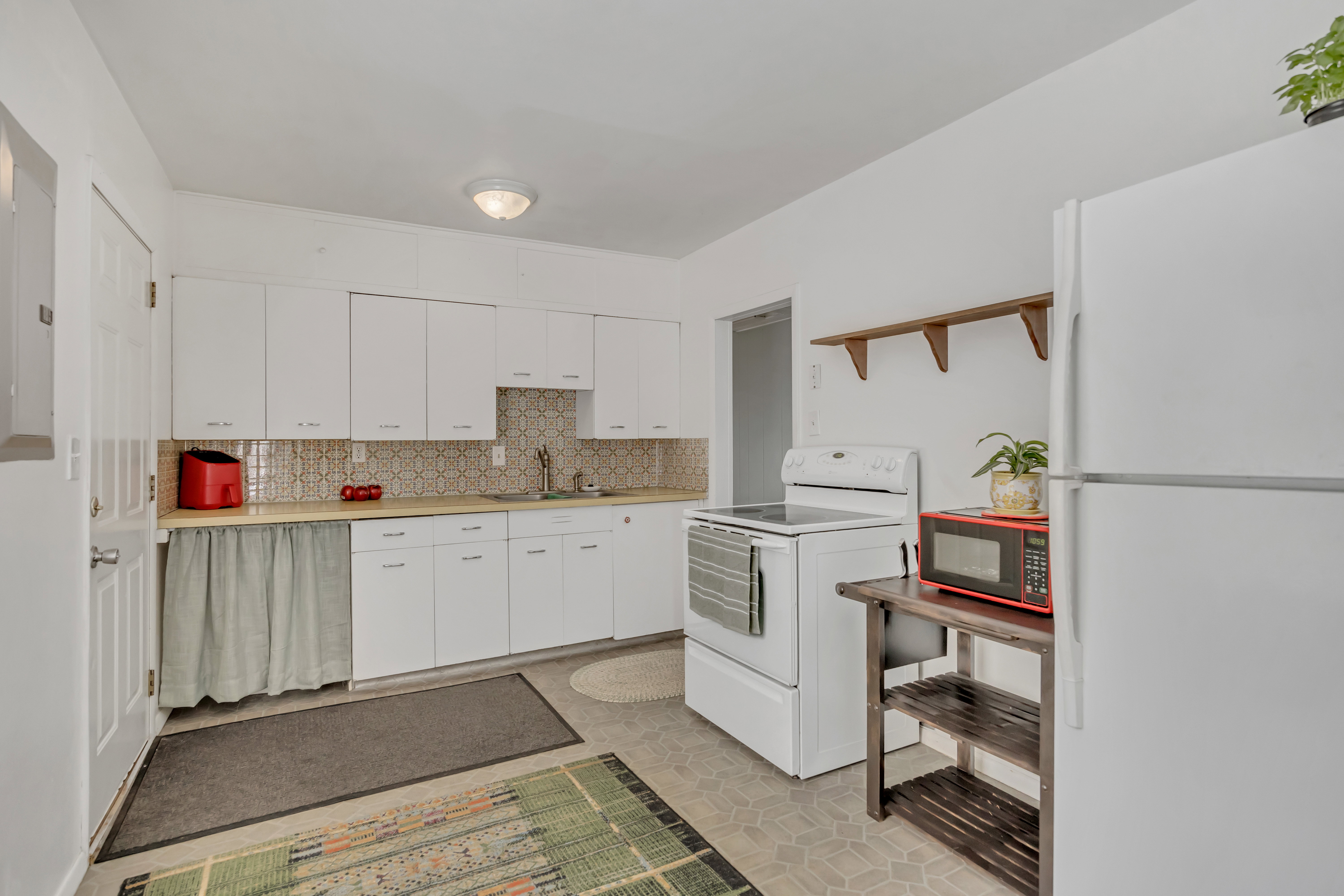 Kitchen featuring white cabinetry, a patterned tile backsplash, a stainless steel sink, and light-toned countertops