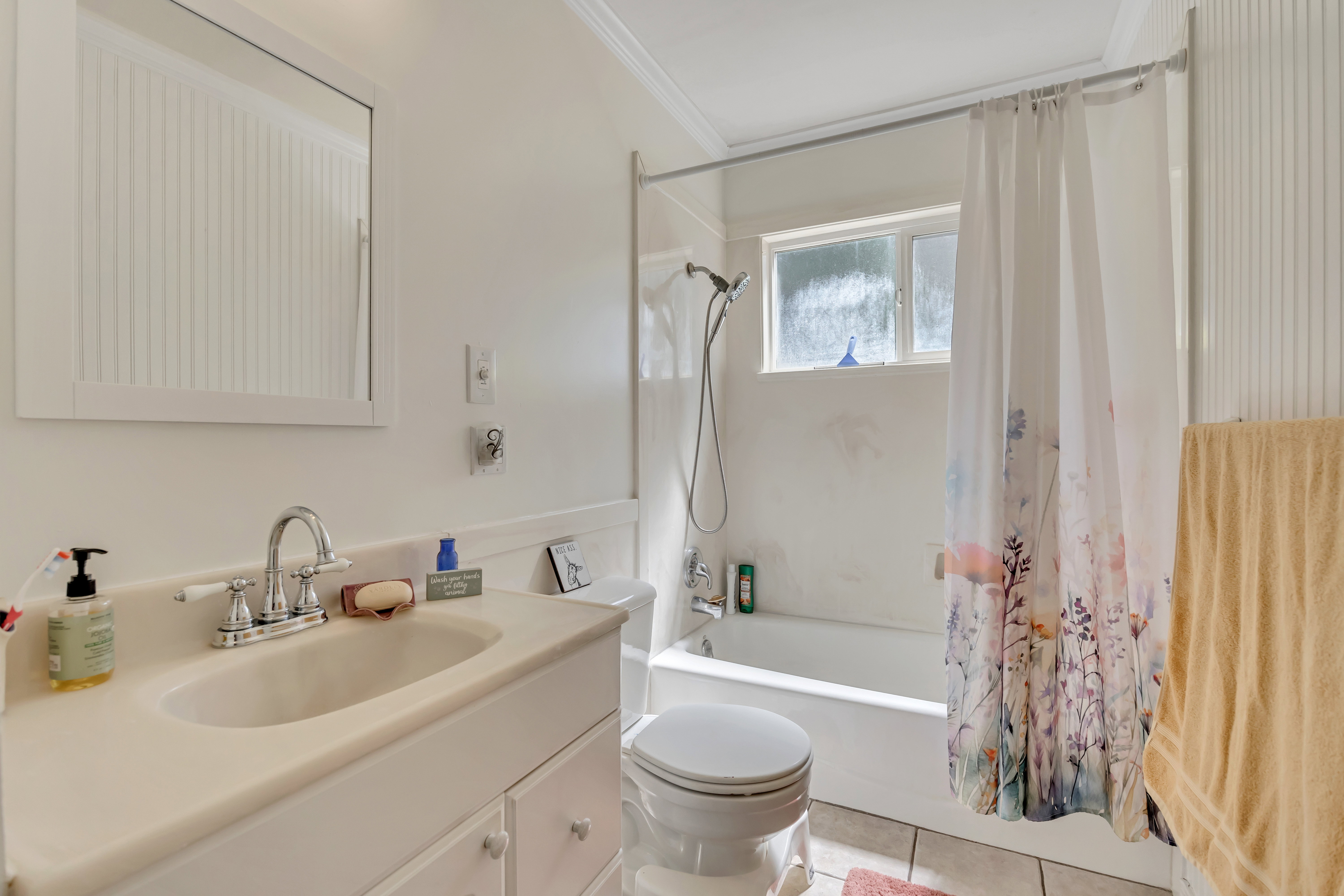 Bathroom featuring a vanity with an integrated sink and chrome faucet, a white toilet, a bathtub with a shower head, and a window for natural light