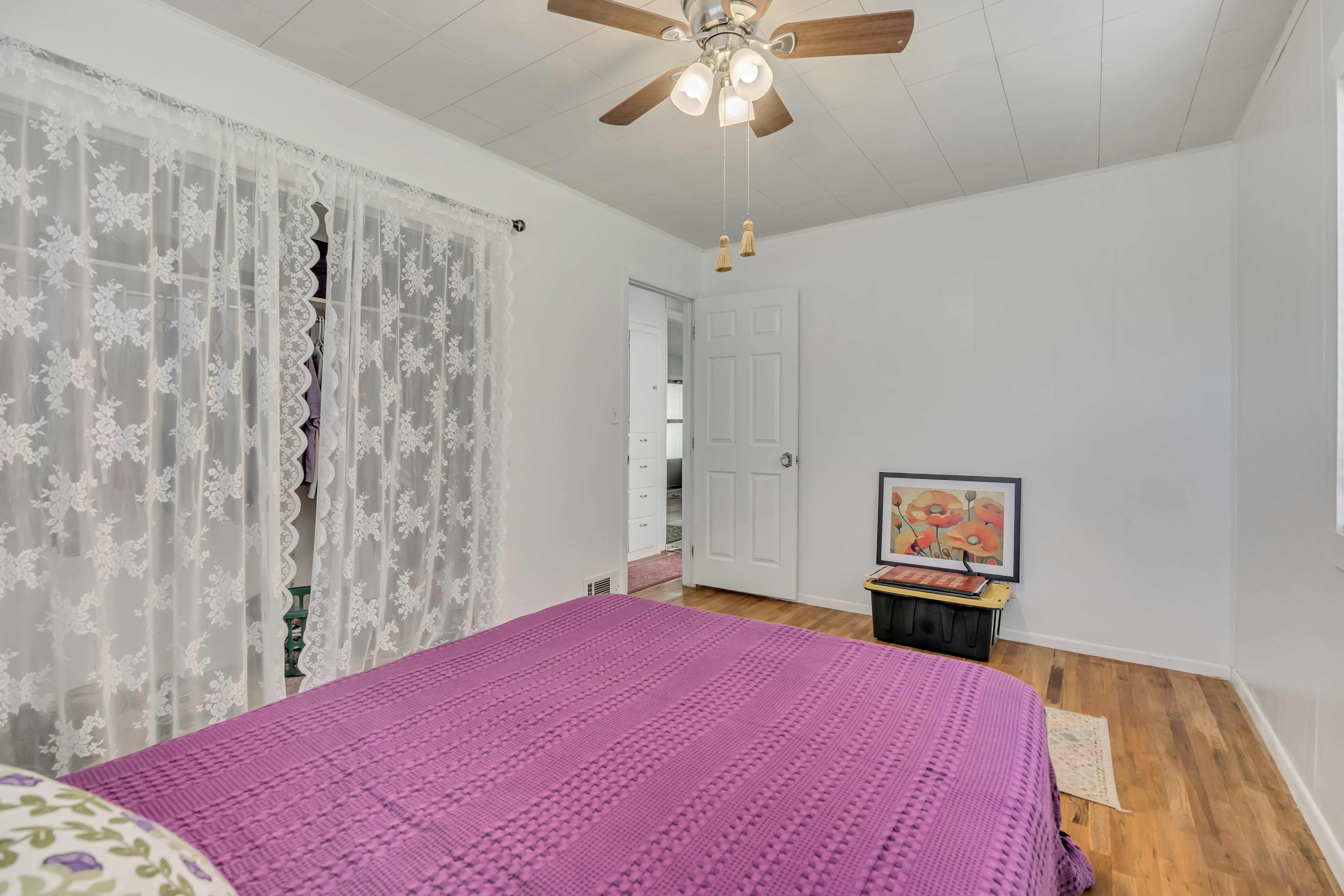 Bright room with wood-finish flooring, a white paneled door, and a ceiling fan with integrated lighting