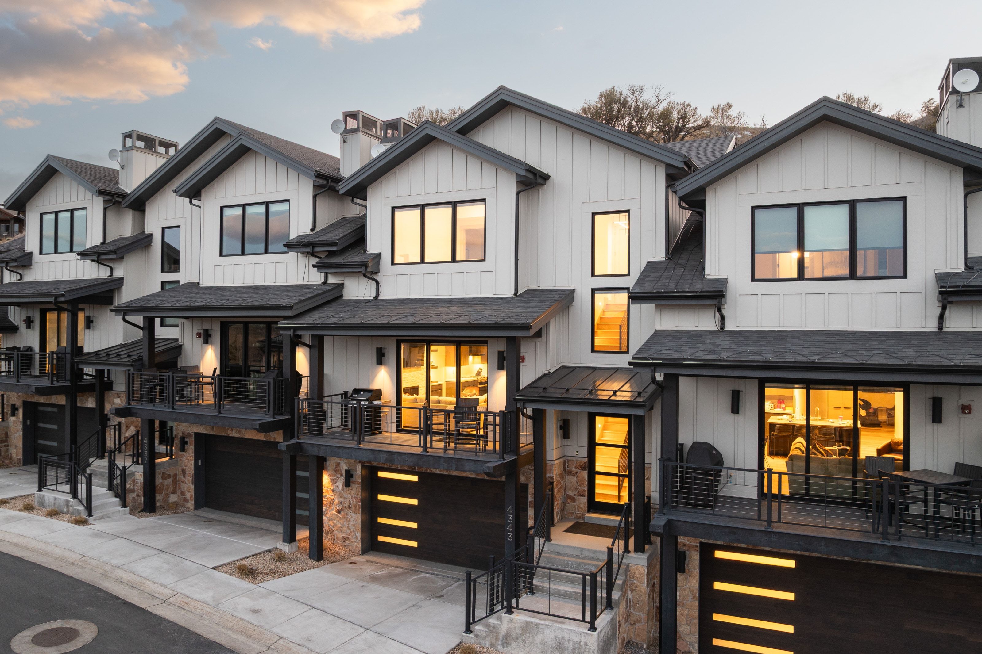 Contemporary townhomes featuring white vertical siding, black trim, and gabled roofs