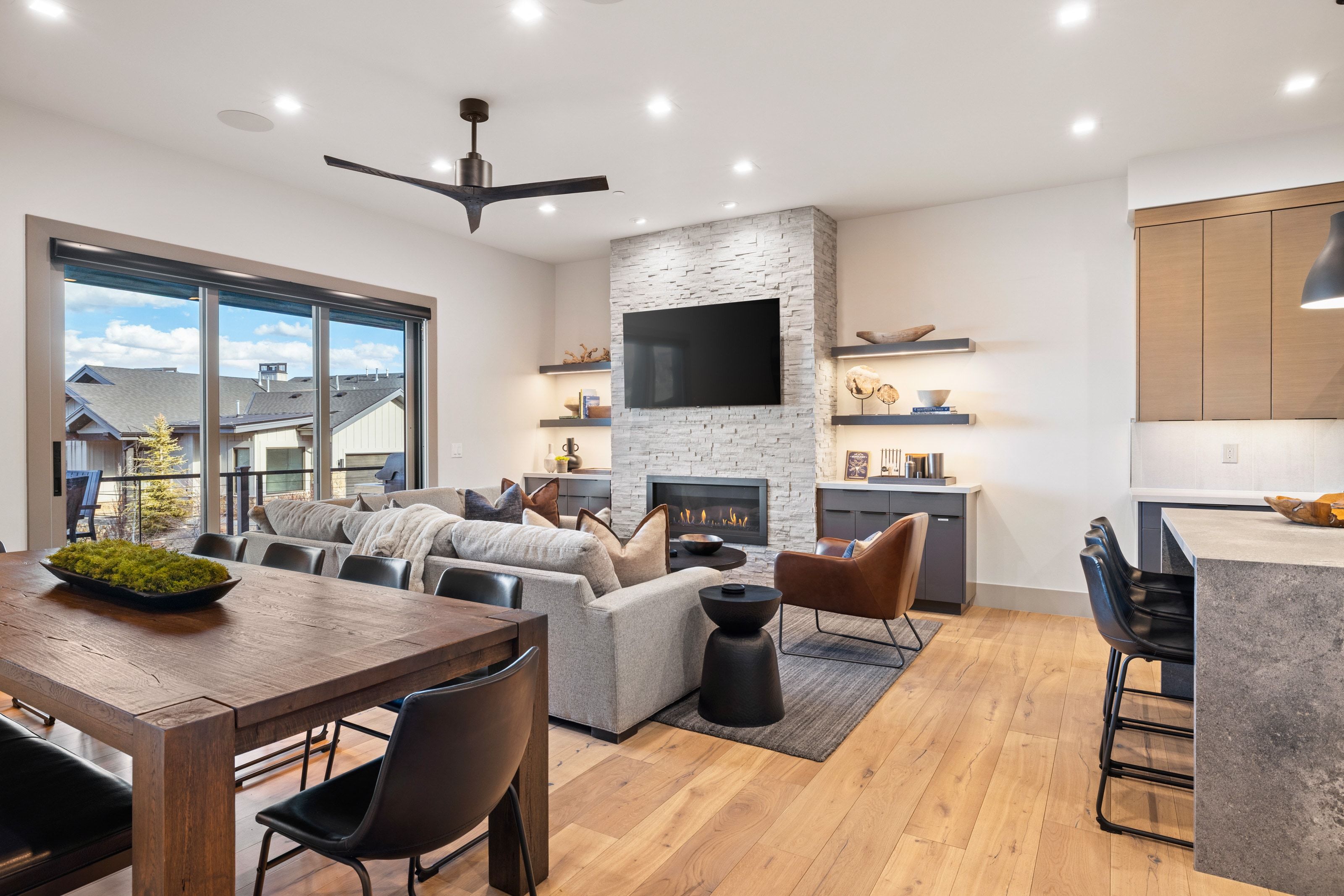 Open-concept living space featuring wood-finish flooring, a stone-clad fireplace, and sliding glass doors