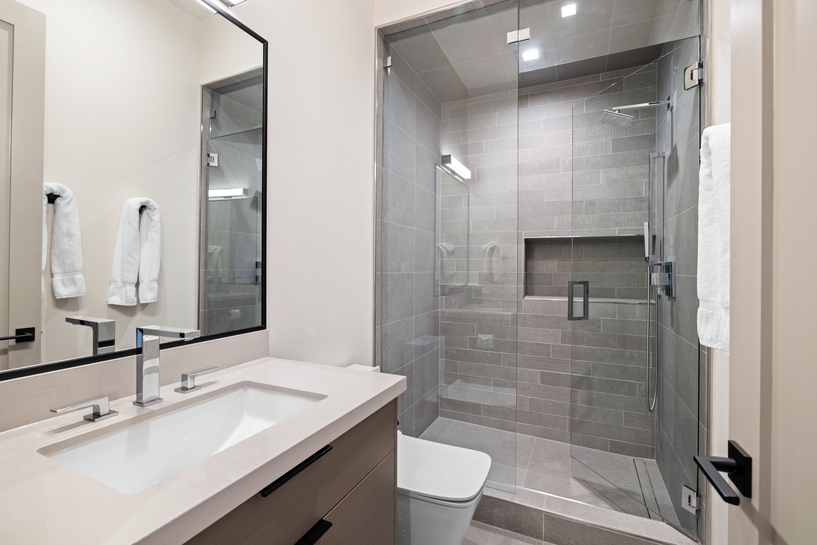 Contemporary bathroom featuring a frameless glass shower enclosure with gray tile surround and built-in niche
