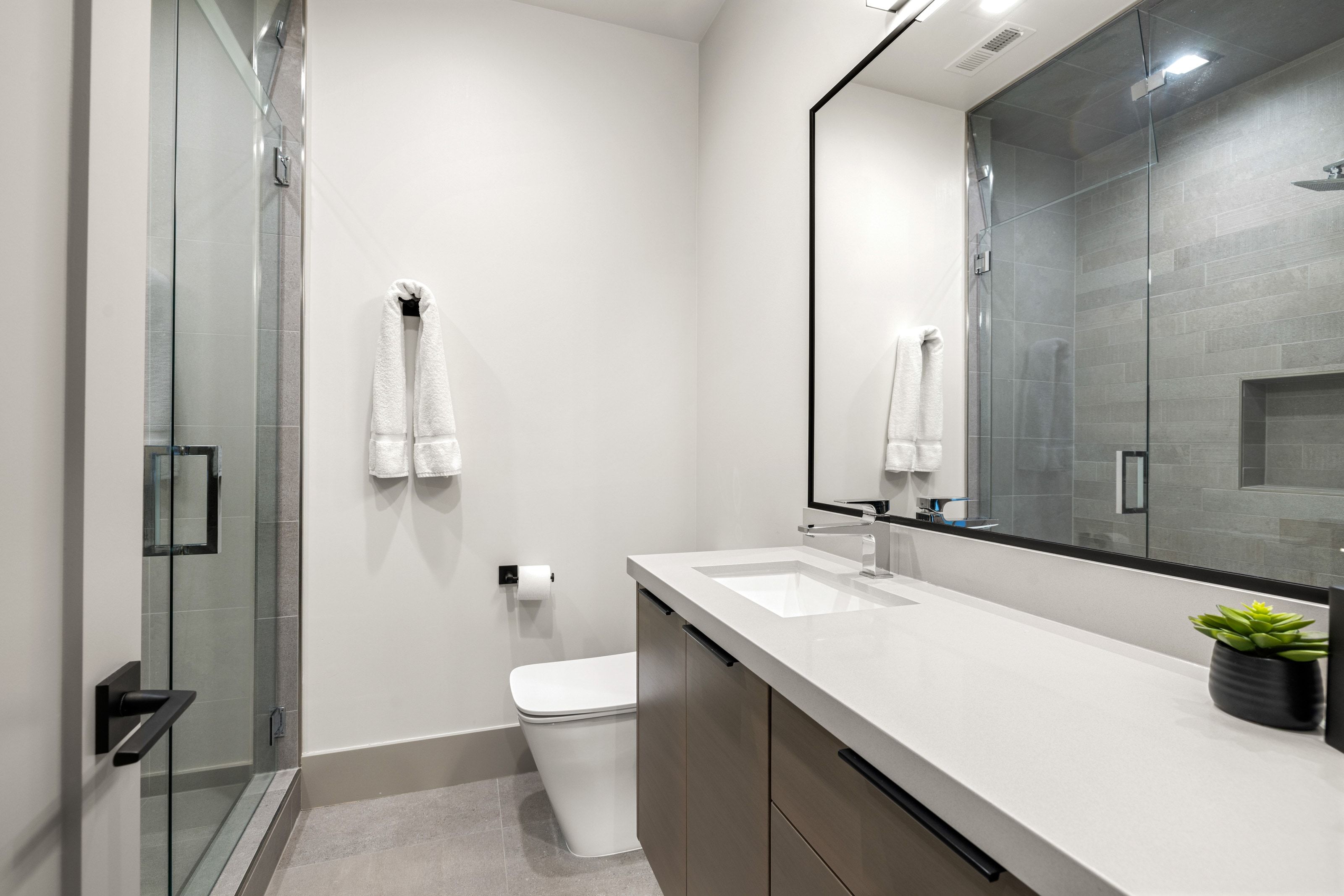 Contemporary bathroom featuring a frameless glass shower enclosure with subway tile surround, a built-in shower niche, and a vanity with an integrated sink and light-colored countertop