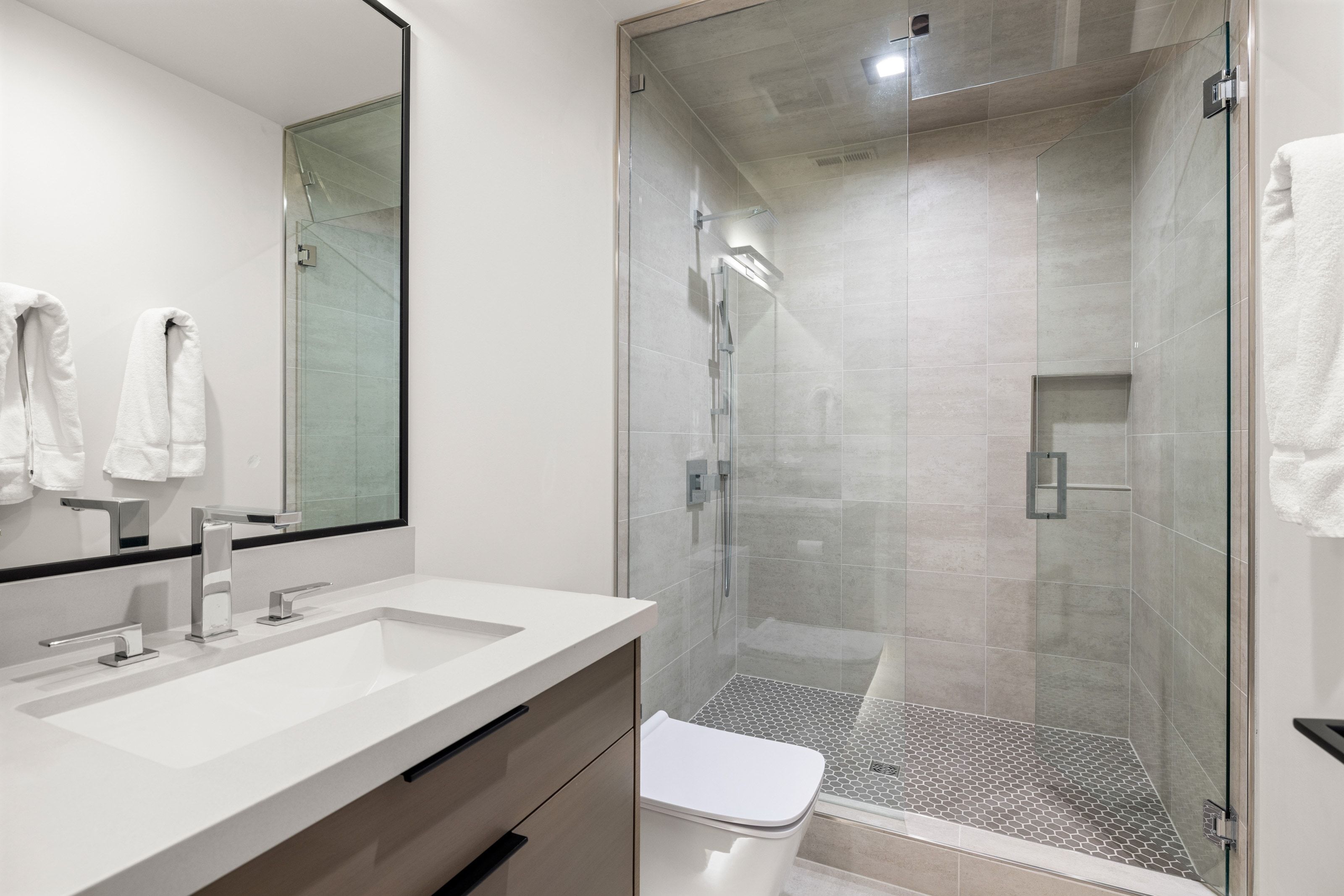 Contemporary bathroom featuring a spacious glass-enclosed shower, a white vanity countertop with an integrated sink, and sleek chrome fixtures