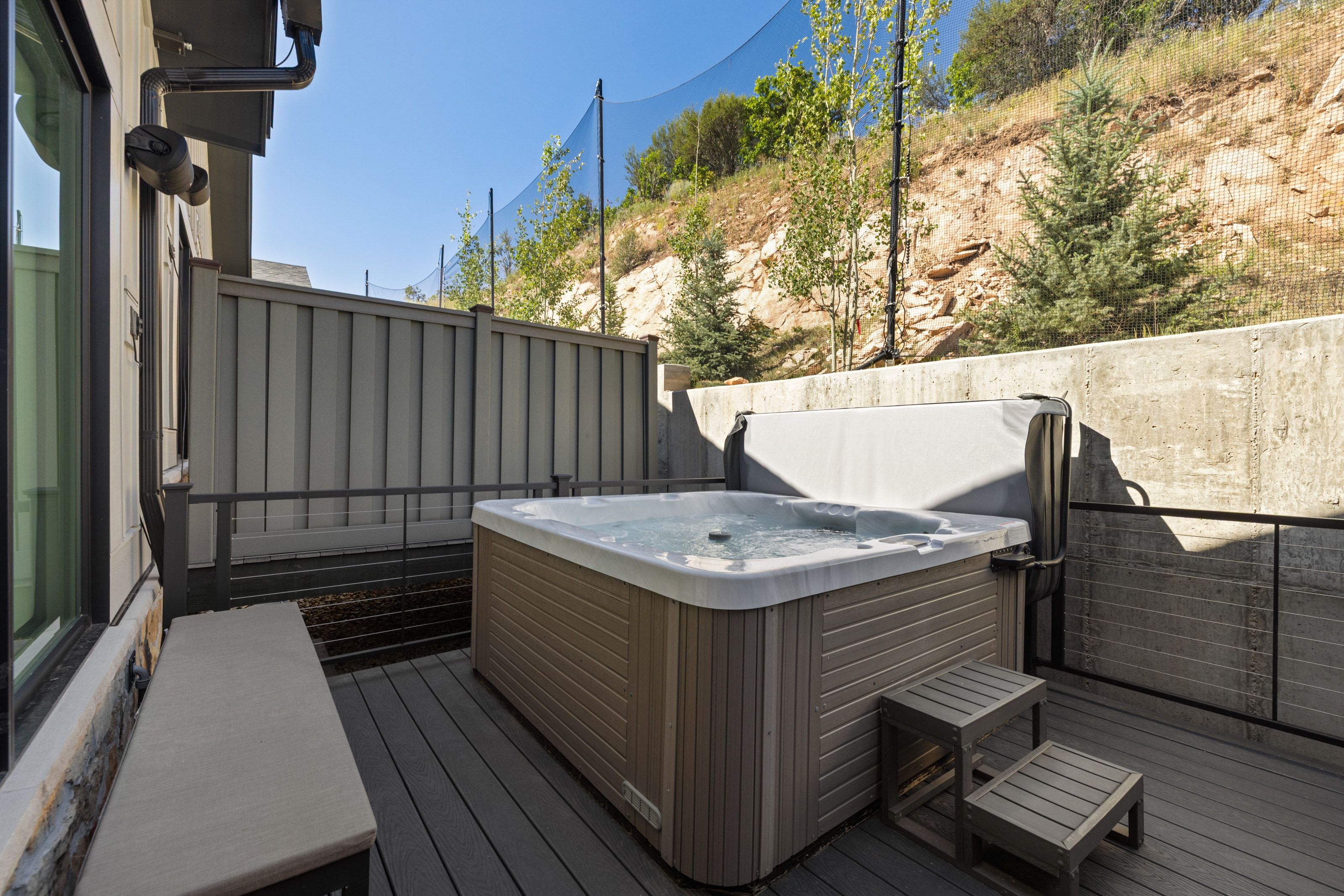 Outdoor patio featuring a built-in hot tub with cover, composite decking, and a low stone wall