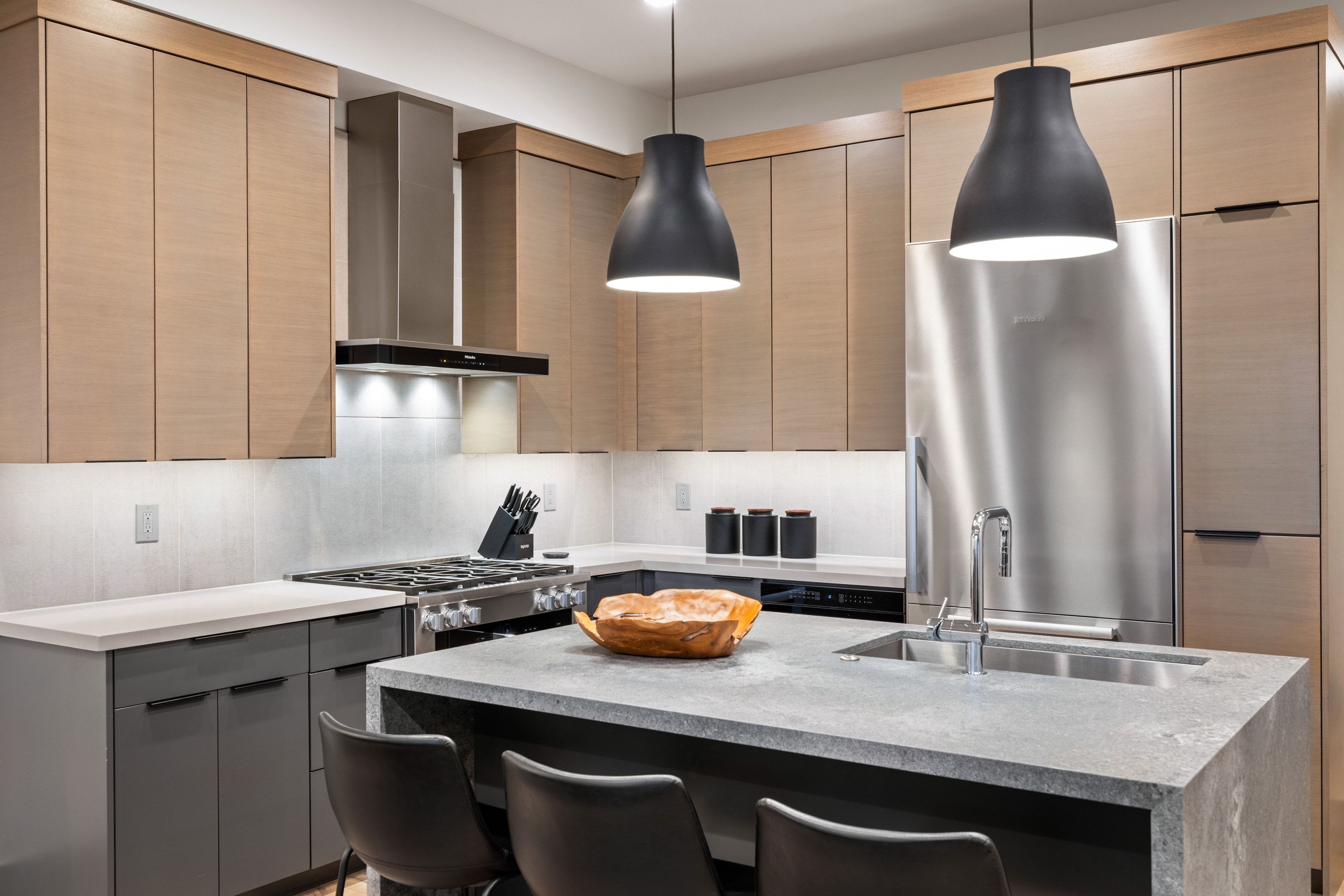 Modern kitchen featuring light wood-finish upper cabinetry, gray lower cabinetry, and stainless steel appliances