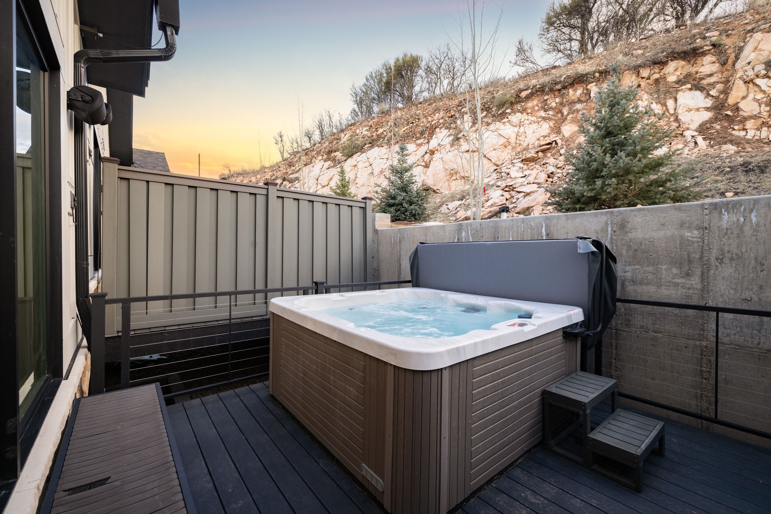 Deck featuring a spa, durable composite decking, privacy fencing, and a concrete retaining wall