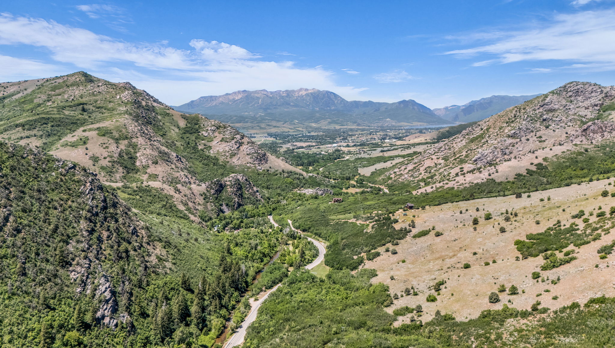 Sweeping mountain landscape featuring a winding road, lush green valleys, distant peaks, and clear blue skies