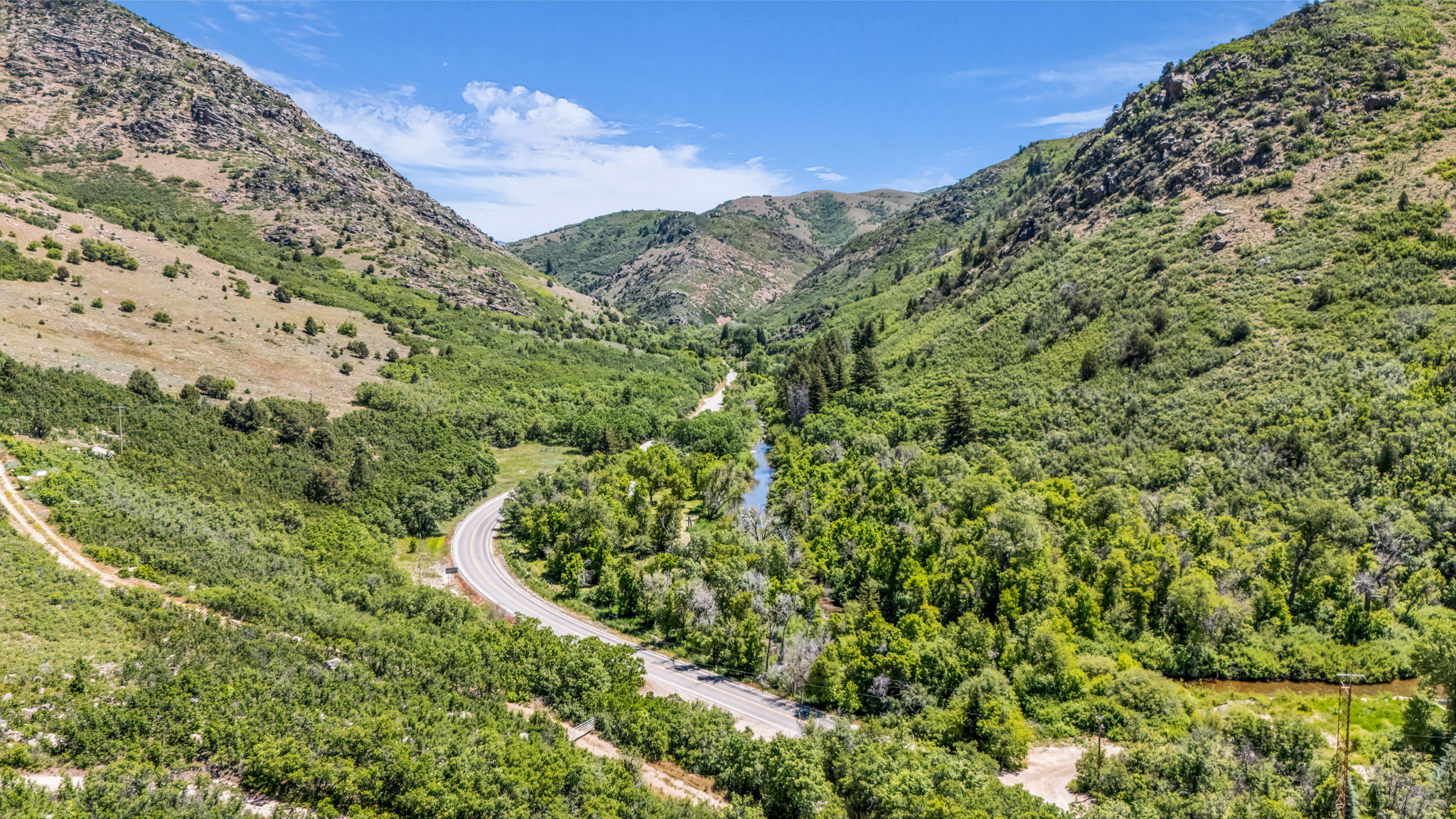 Mountainous landscape featuring a winding road, lush green foliage, and a prominent river