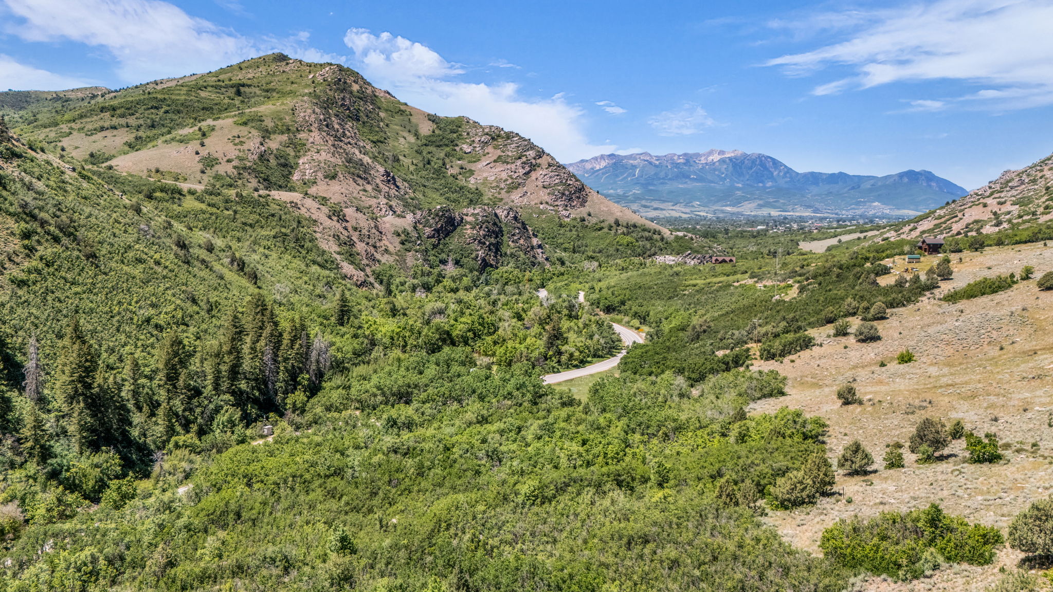 Expansive mountainous landscape featuring diverse foliage, distant mountain ranges, and a winding road