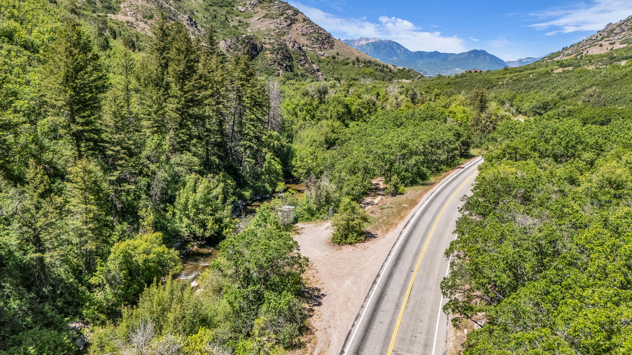 Mountainous landscape featuring a paved road, lush green trees, and a visible stream