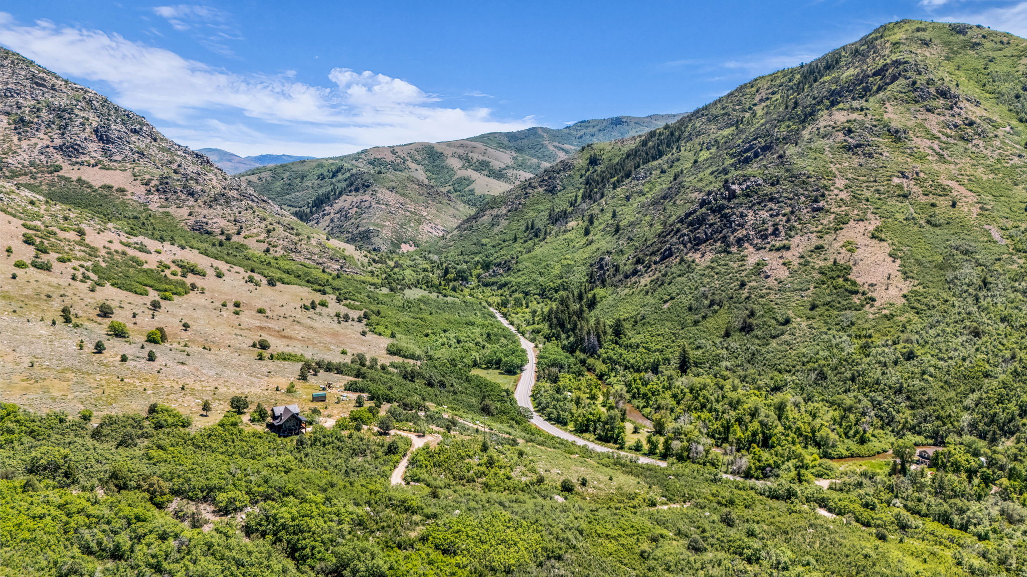 Mountain landscape with a winding road and a single structure nestled among lush green foliage