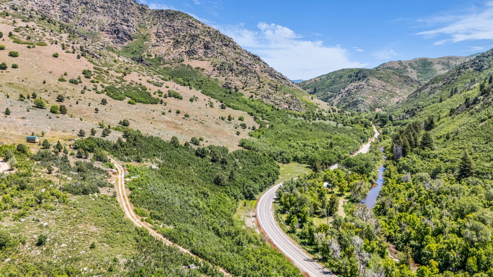 Expansive mountain terrain featuring a paved road, a winding river, and abundant green foliage