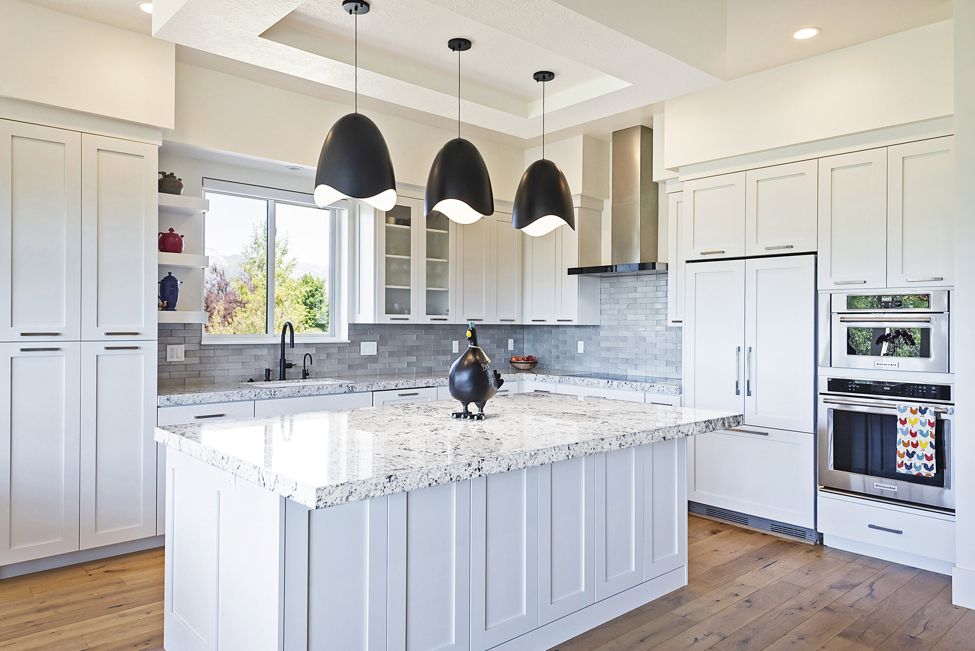 Bright kitchen featuring white cabinetry, a large center island with a speckled countertop, integrated stainless steel appliances, and wood-finish flooring