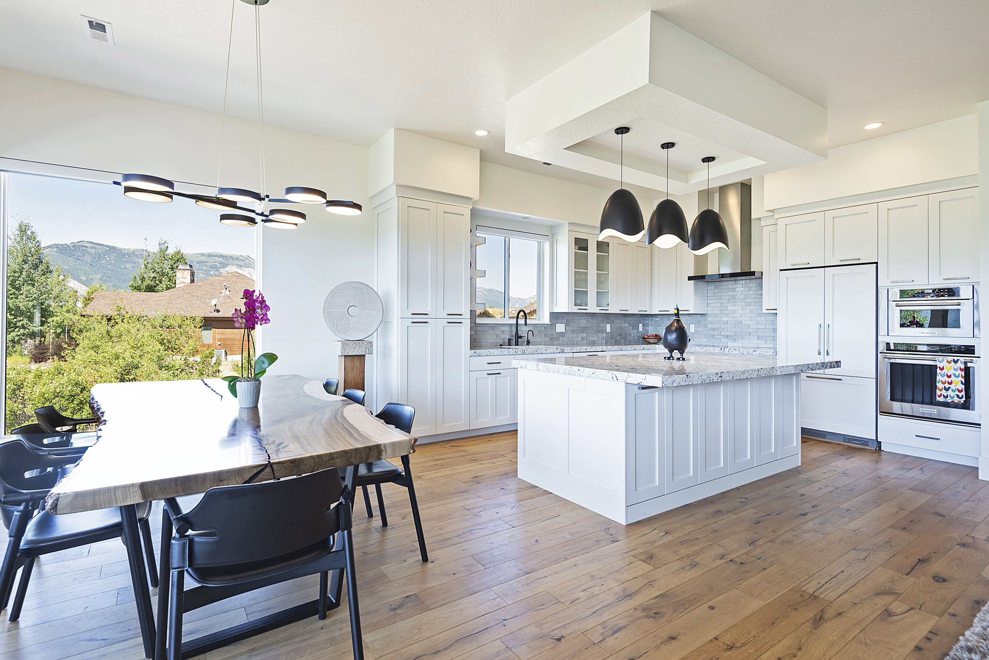 Open-concept kitchen and dining area featuring wide-plank wood-finish flooring, white cabinetry, a central island with a stone countertop, and stainless steel appliances