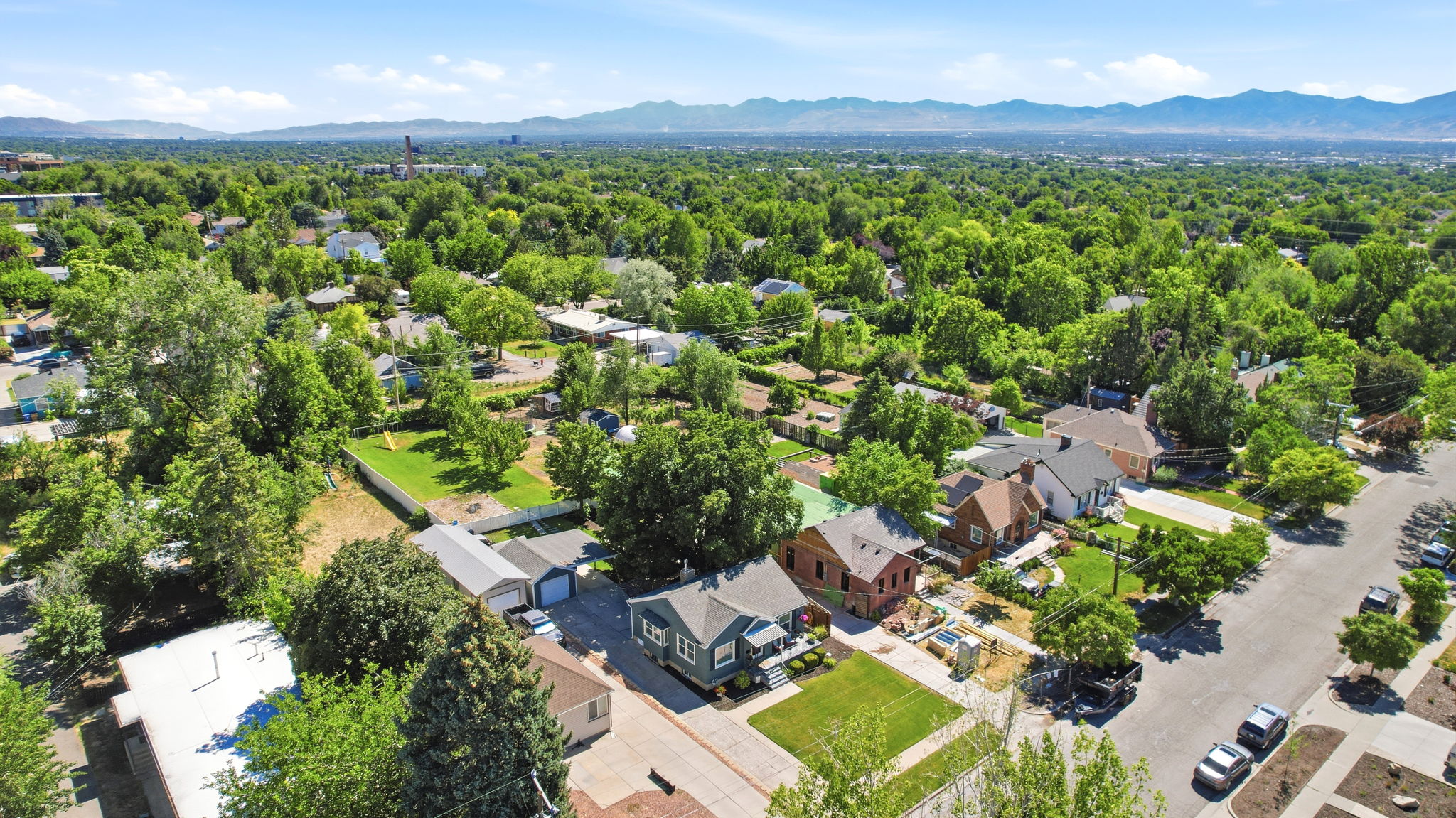 Aerial perspective showcasing a residential neighborhood with abundant mature trees and distant mountain ranges