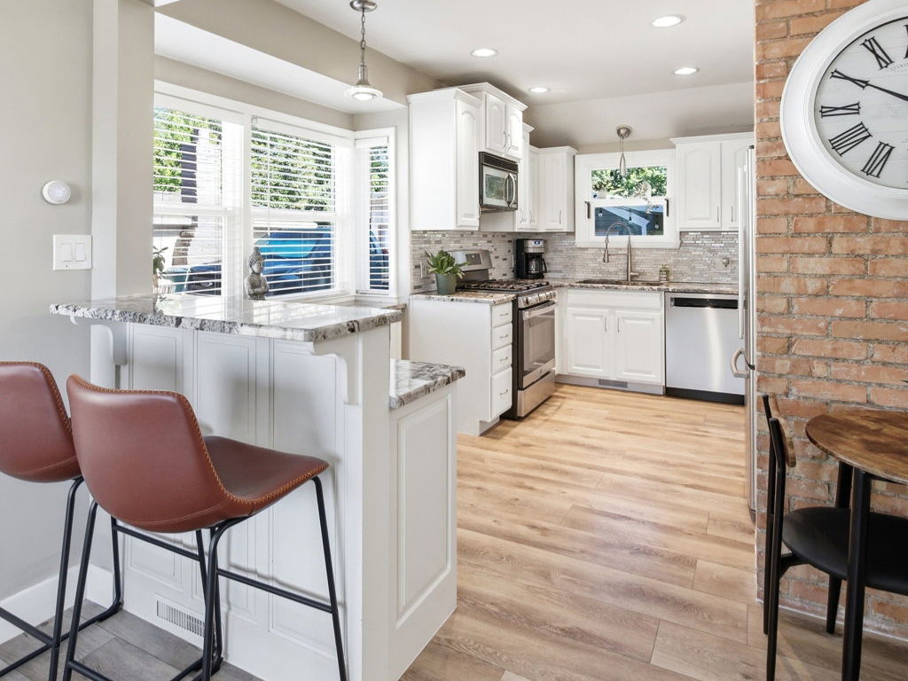 Kitchen featuring wood-finish flooring, white cabinetry, stainless steel appliances, and a granite-topped breakfast bar