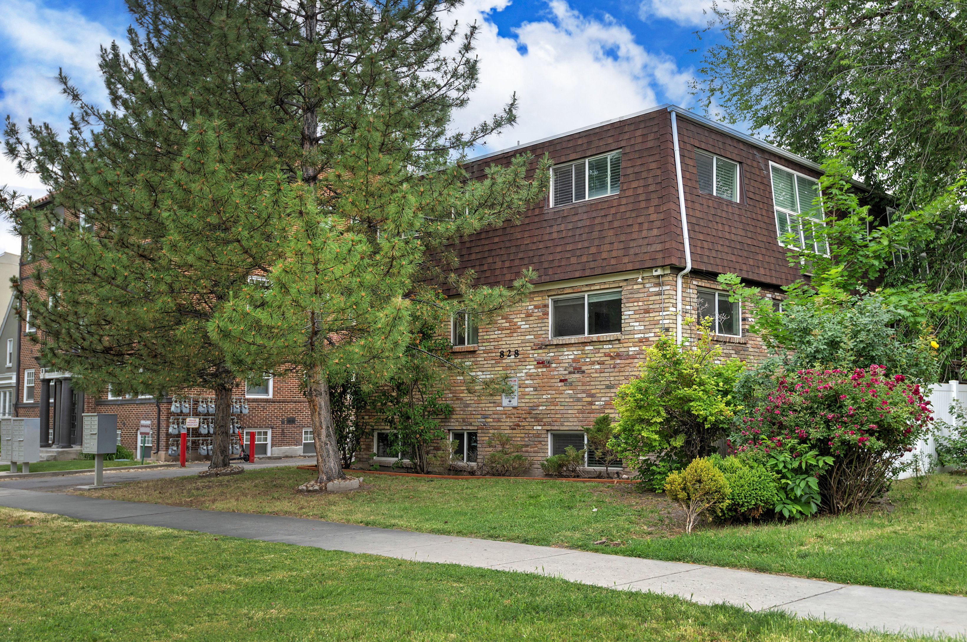 Brick facade building with a mansard roof, featuring an established lawn and mature trees