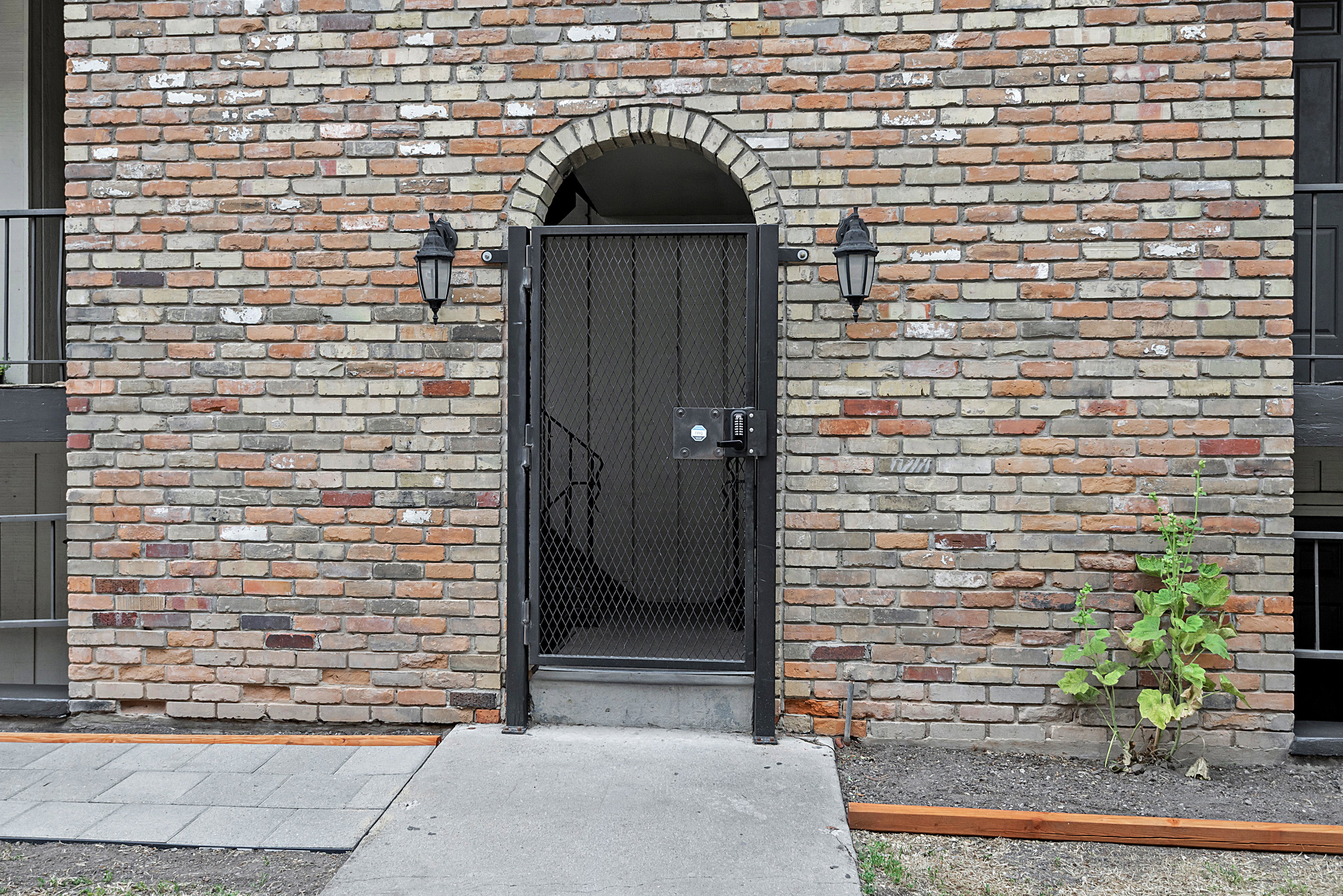Brick exterior featuring an arched entryway, decorative metal security gate, and dual exterior sconces
