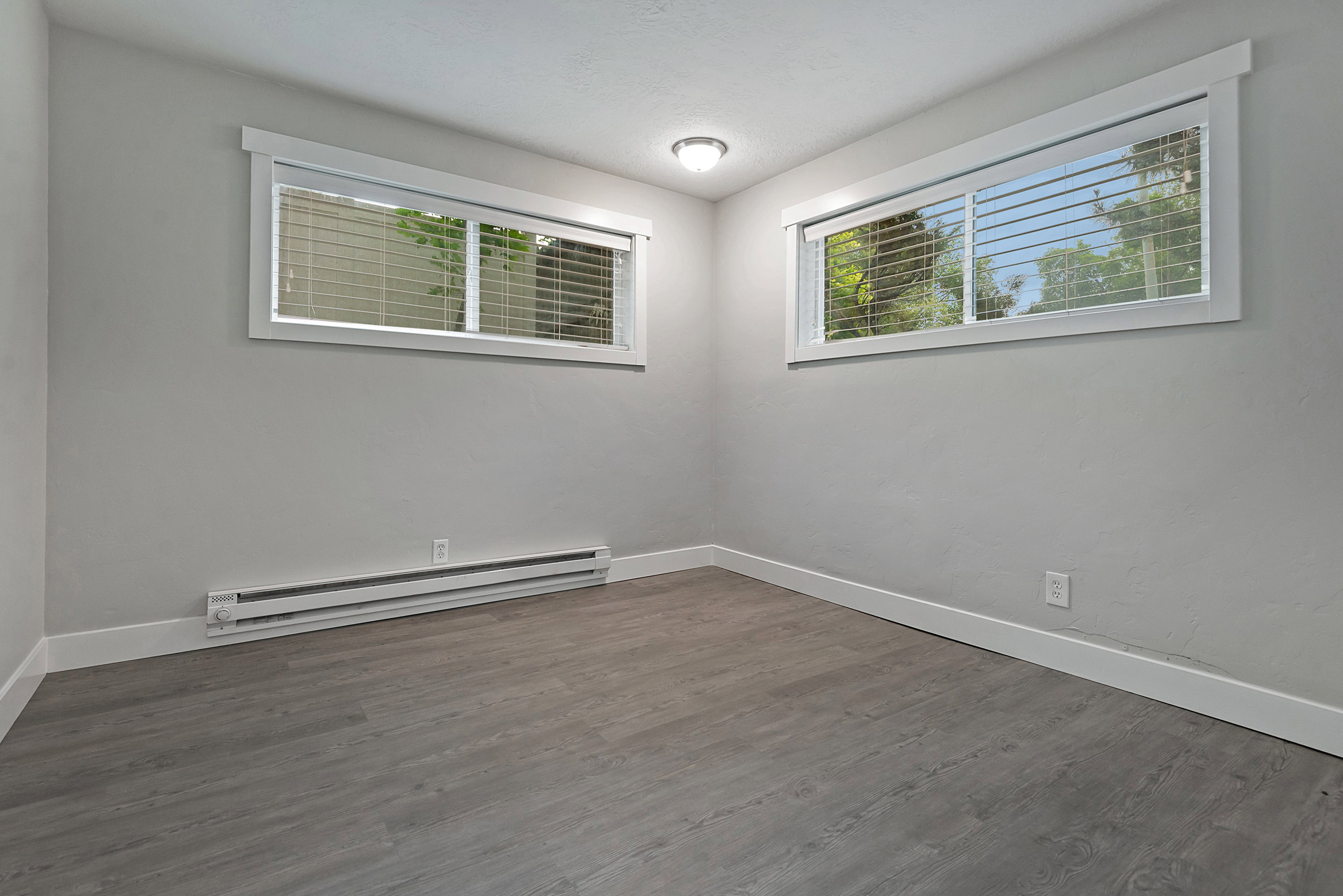 Room featuring two horizontal windows with blinds, wood-finish flooring, and white baseboards