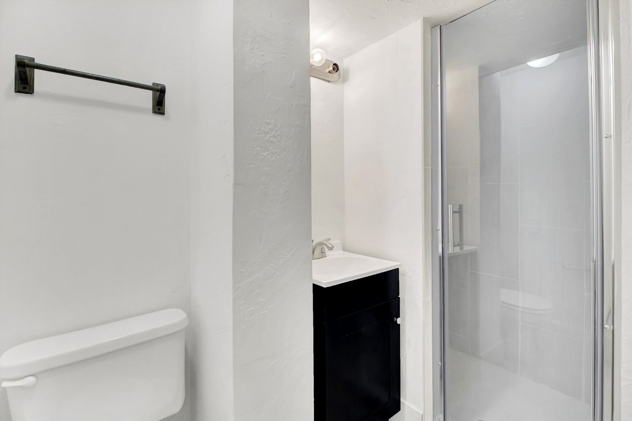 Contemporary basement bathroom featuring a glass-enclosed shower, white tile, a vanity with a white countertop, and a chrome faucet,
