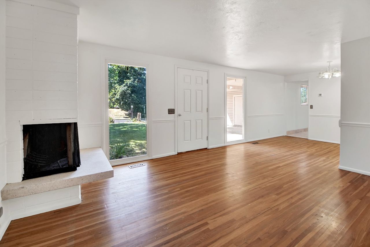 Spacious open concept room featuring hardwood flooring and a white painted brick fireplace.