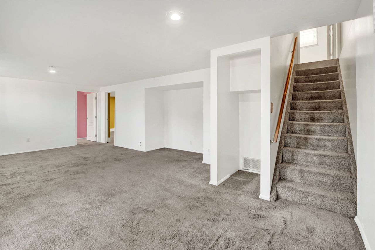 Basement living space with carpeted staircase with a wood handrail, recessed lighting, and white walls