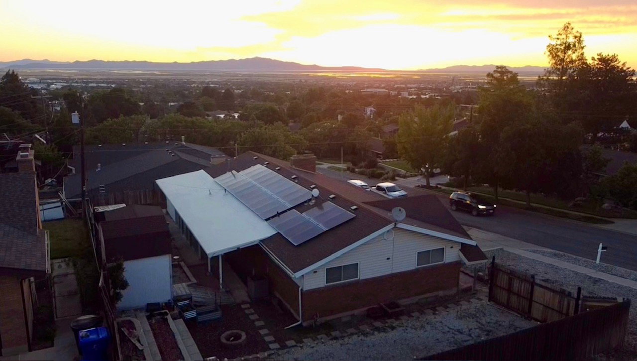 Residential property featuring multiple roof-mounted solar panels, a covered patio extension, and a terraced backyard area
