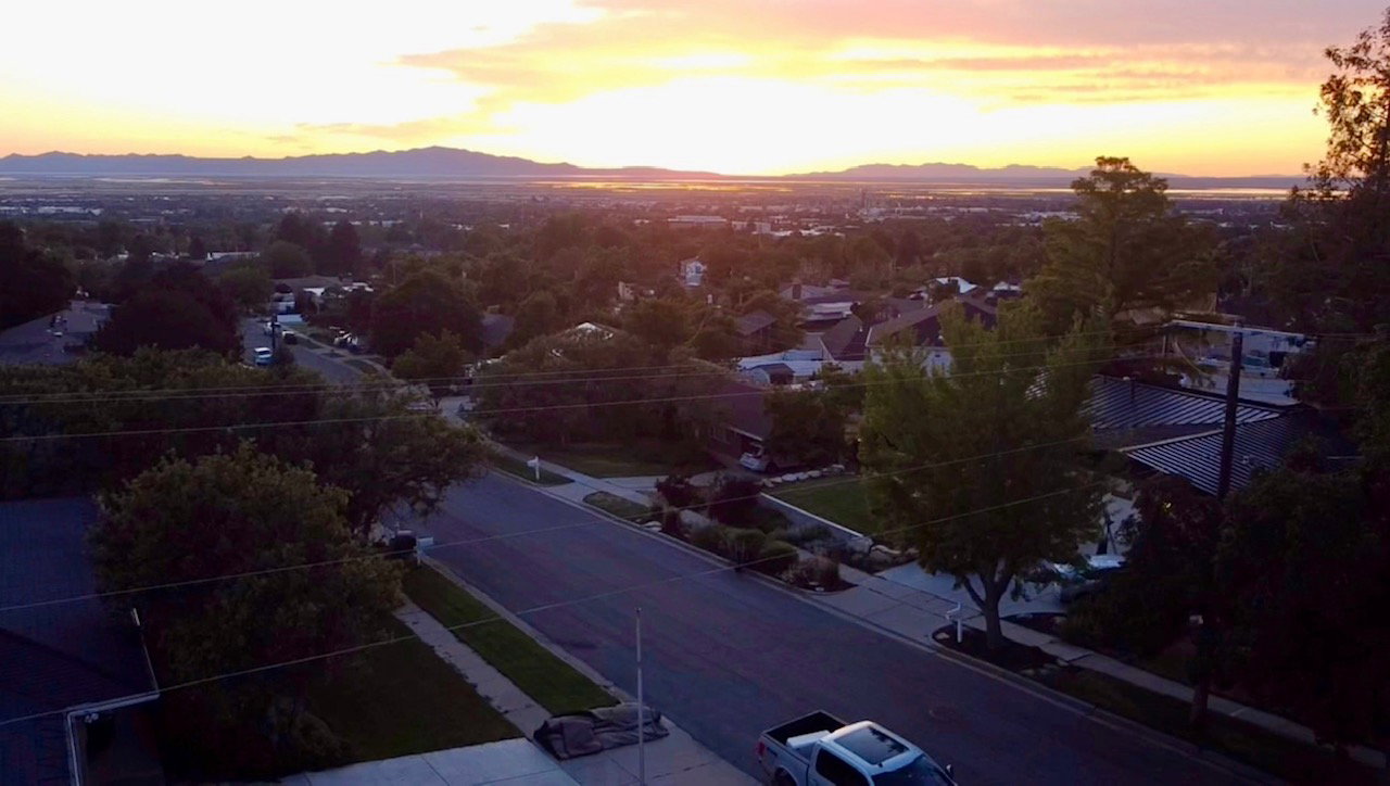 Expansive aerial perspective showcasing a residential neighborhood with distant mountains and a body of water under a twilight sky