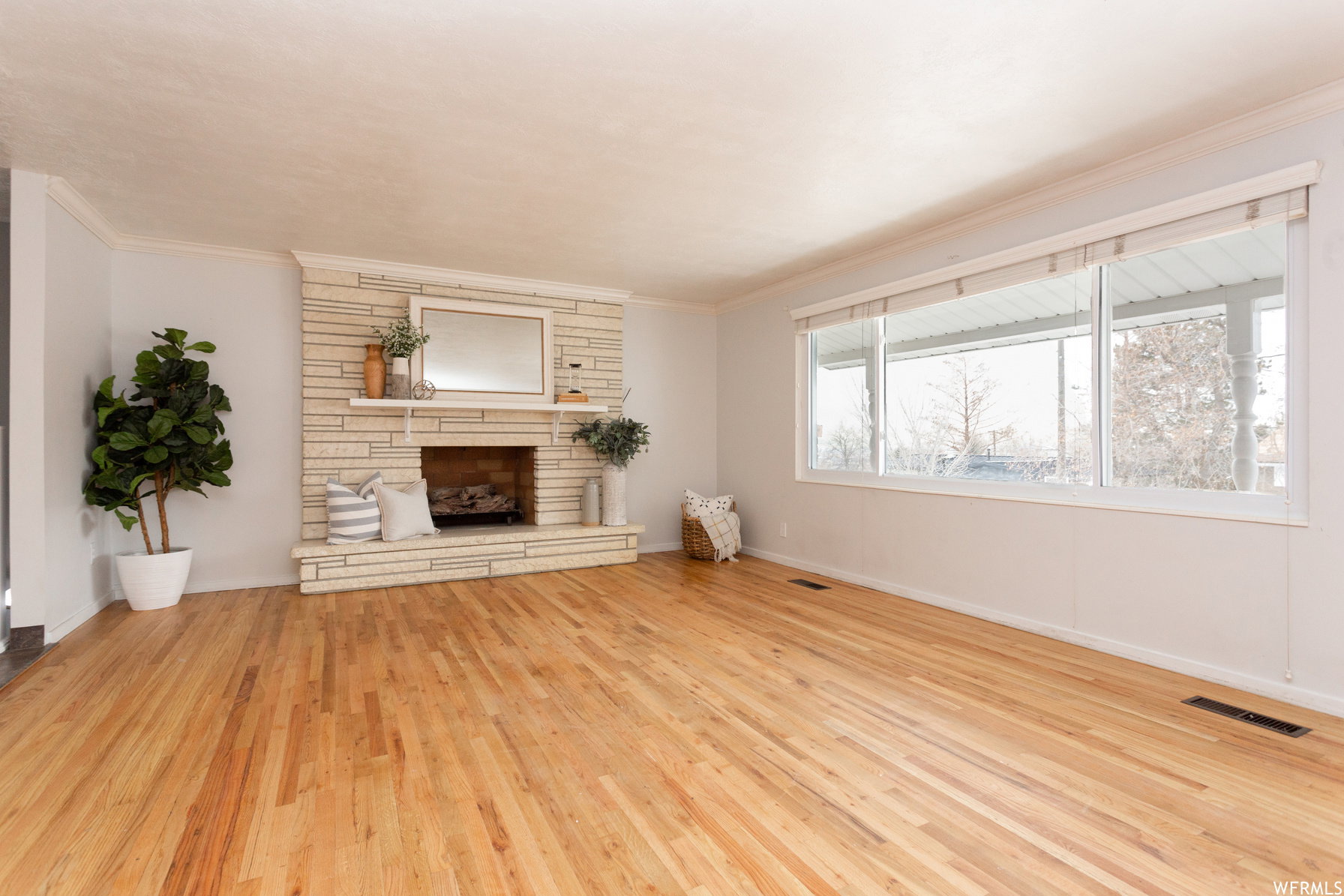 Spacious room featuring wood-finish flooring, a stacked stone fireplace with hearth, and extensive natural light from multiple windows