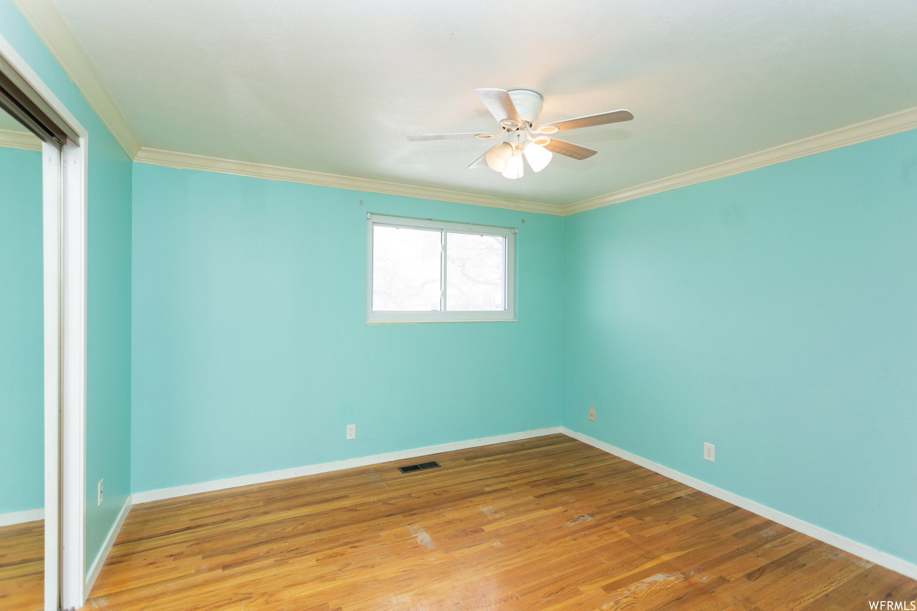 Spacious interior room featuring wood-finish flooring, a ceiling fan with integrated lighting, a window providing natural light, and crown molding