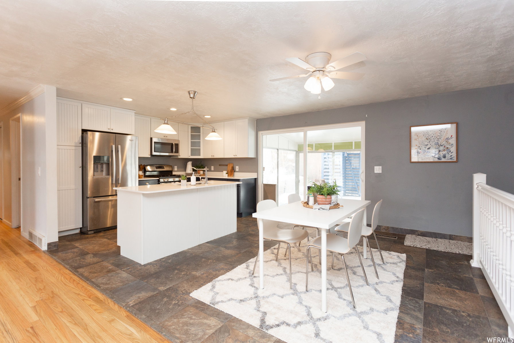 Open-concept kitchen and dining area featuring white cabinetry, stainless steel appliances, a center island with pendant lighting, and a sliding glass door