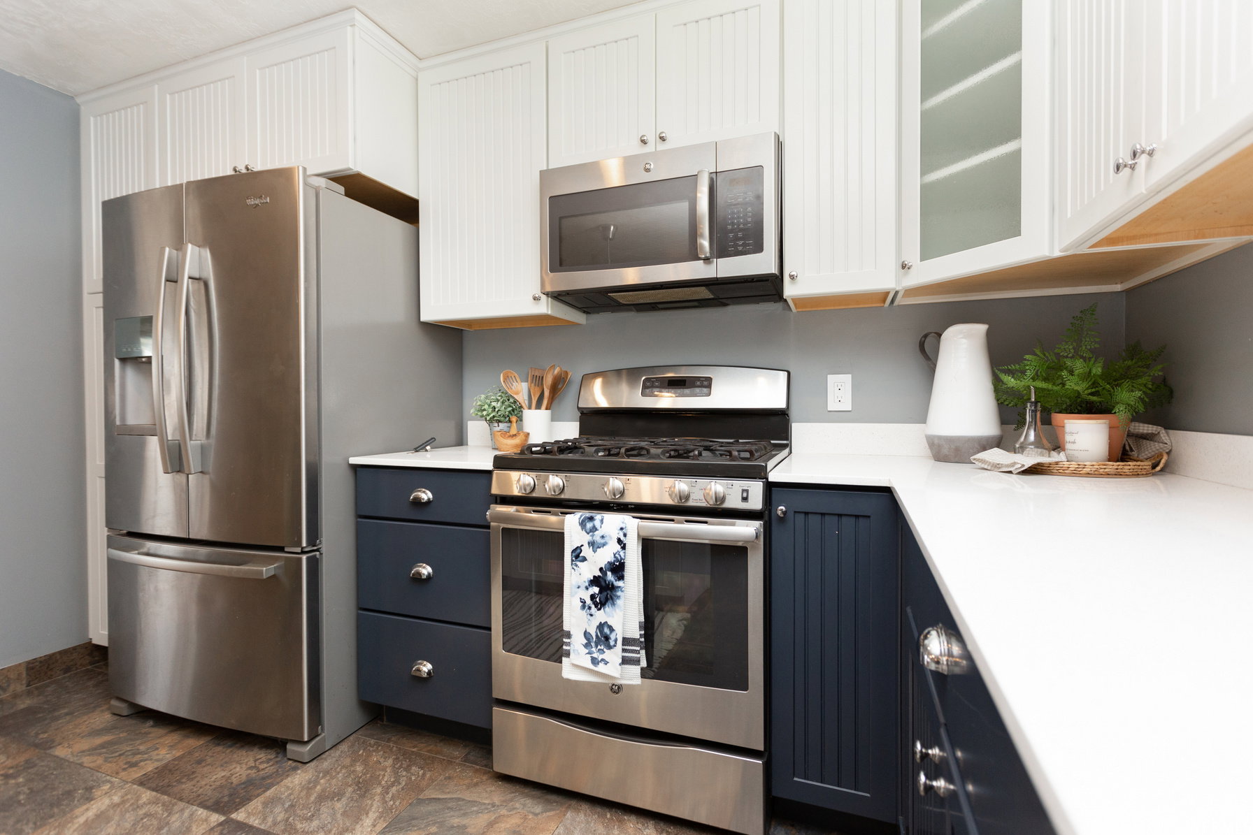 Contemporary kitchen featuring stainless steel appliances, white quartz countertops, two-tone cabinetry with white upper cabinets and navy lower cabinets, and wood-finish flooring