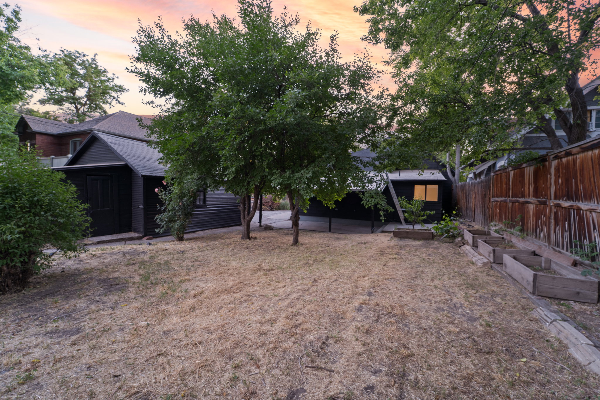 Spacious backyard featuring multiple mature trees, a wooden privacy fence, and a series of terraced raised garden beds